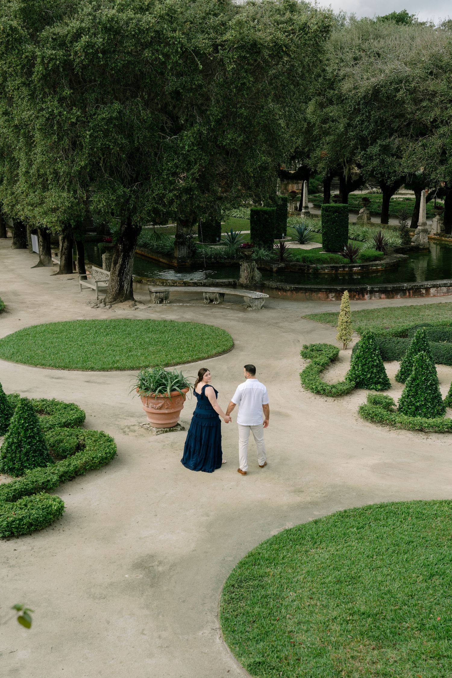 A series of winding dirt paths through a peaceful garden with manicured hedges and tall trees create serene walkways.