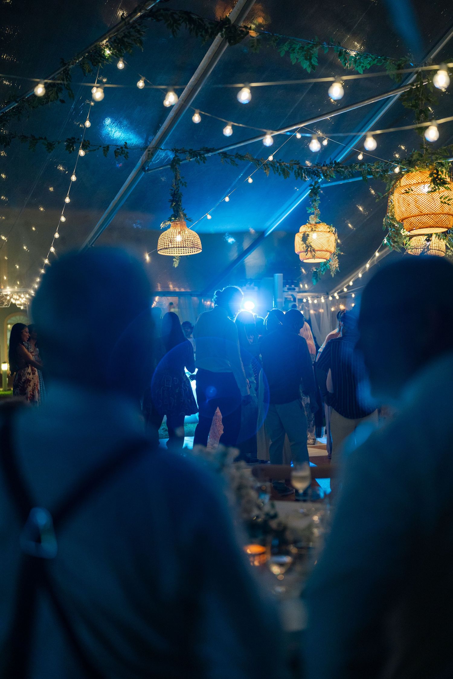 Guests dancing under string lights and hanging lanterns inside a beautifully decorated event tent at night.