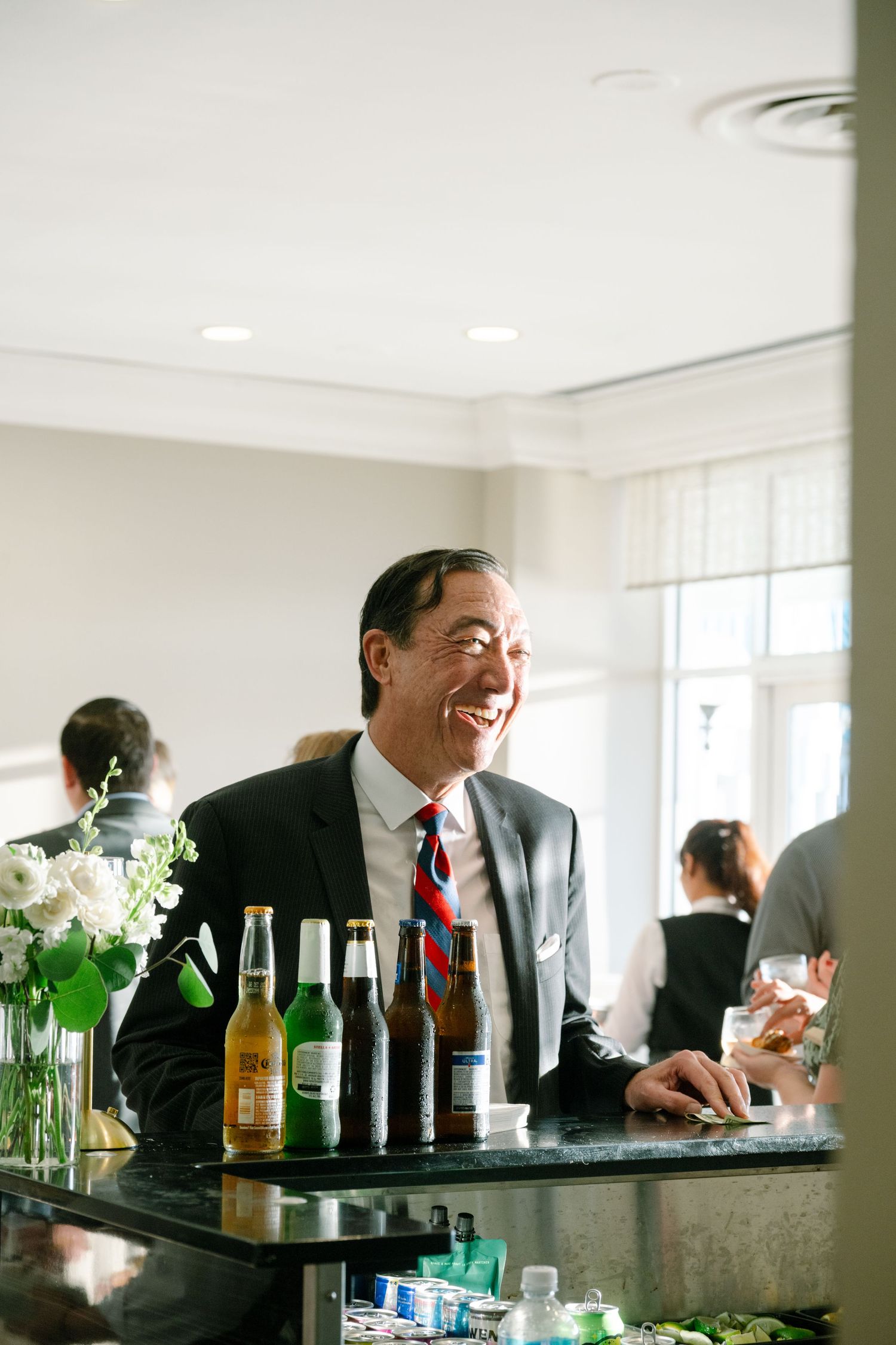 Wedding reception bar setup with bottles and guests enjoying drinks.