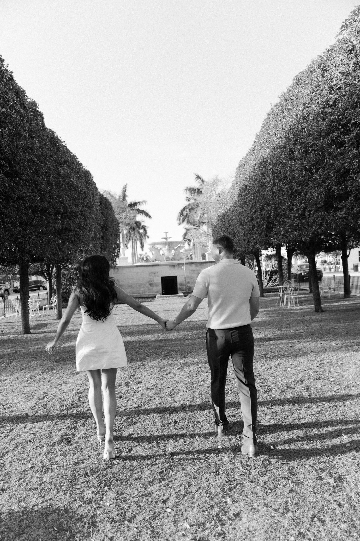 A black and white image shows people walking together across a grassy field on a sunny day.