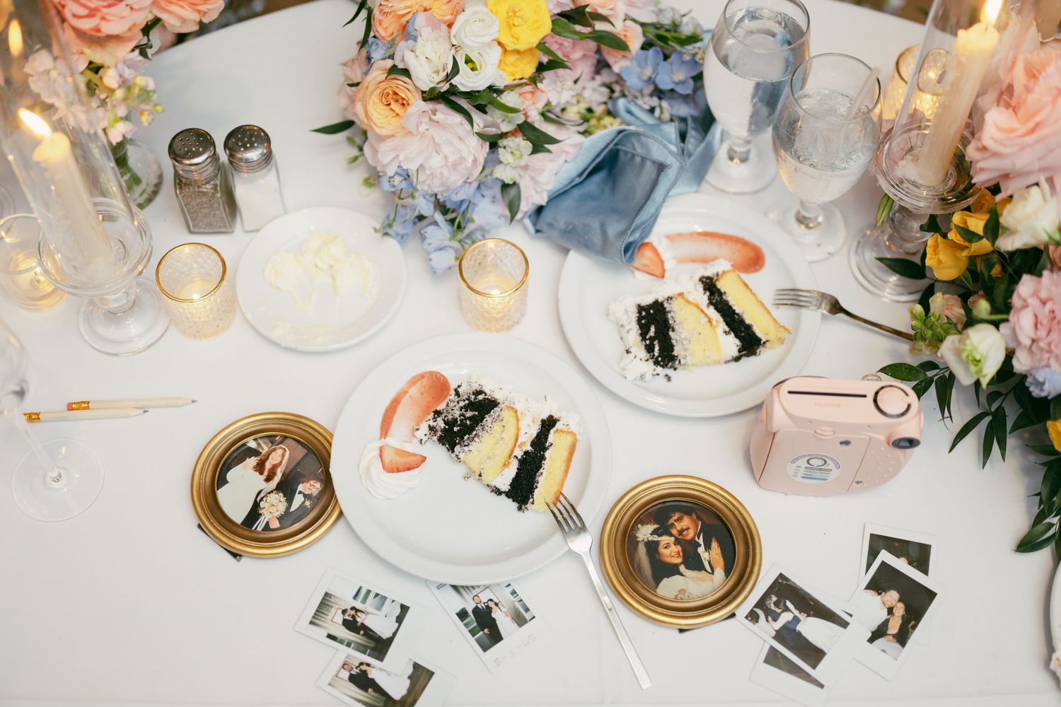 An elegant wedding reception table setting with plated meals, floral arrangements, and vintage photos scattered around.