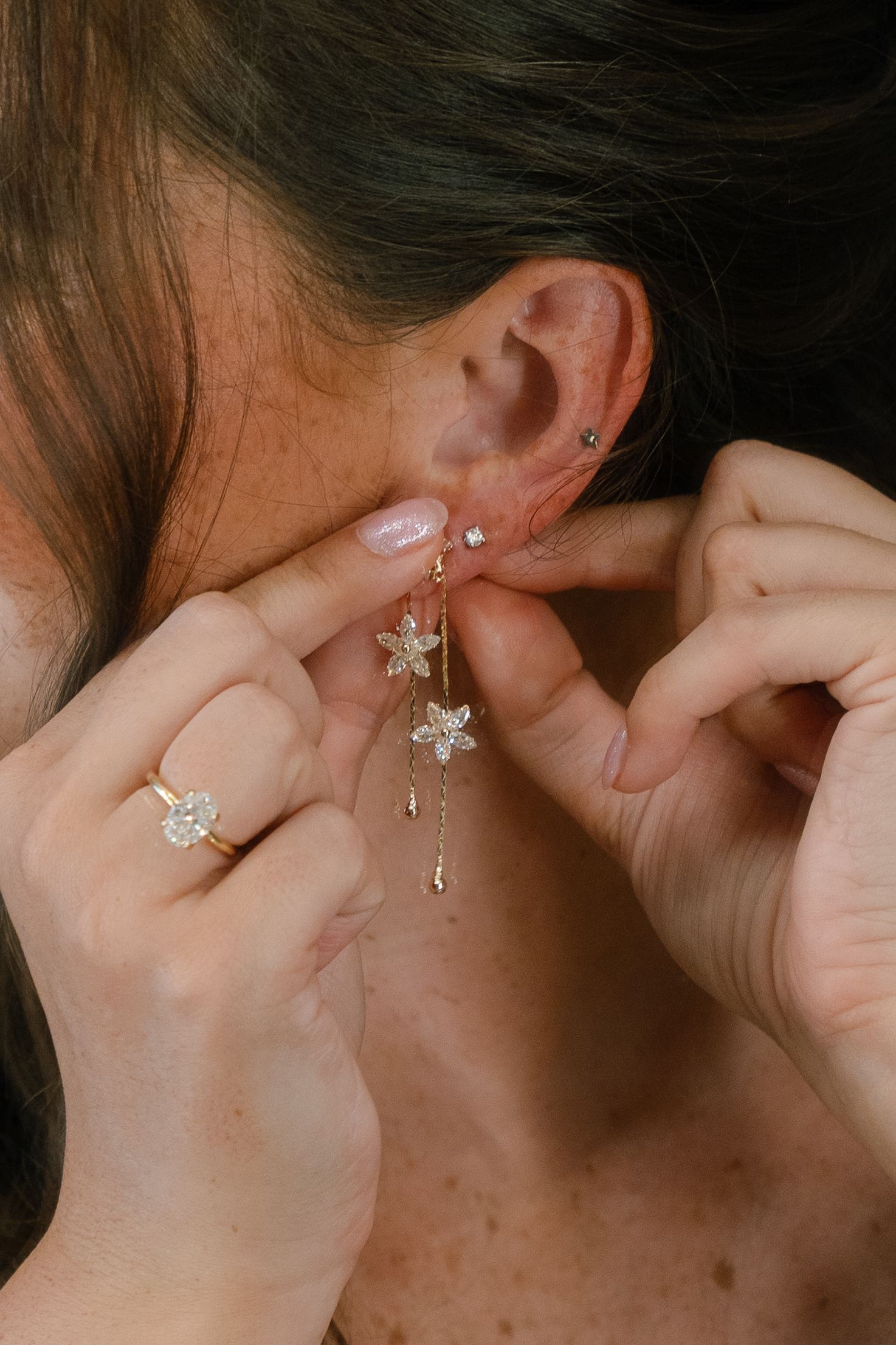 The image shows a close-up view of a person's ear with a pierced earring and long dark hair.