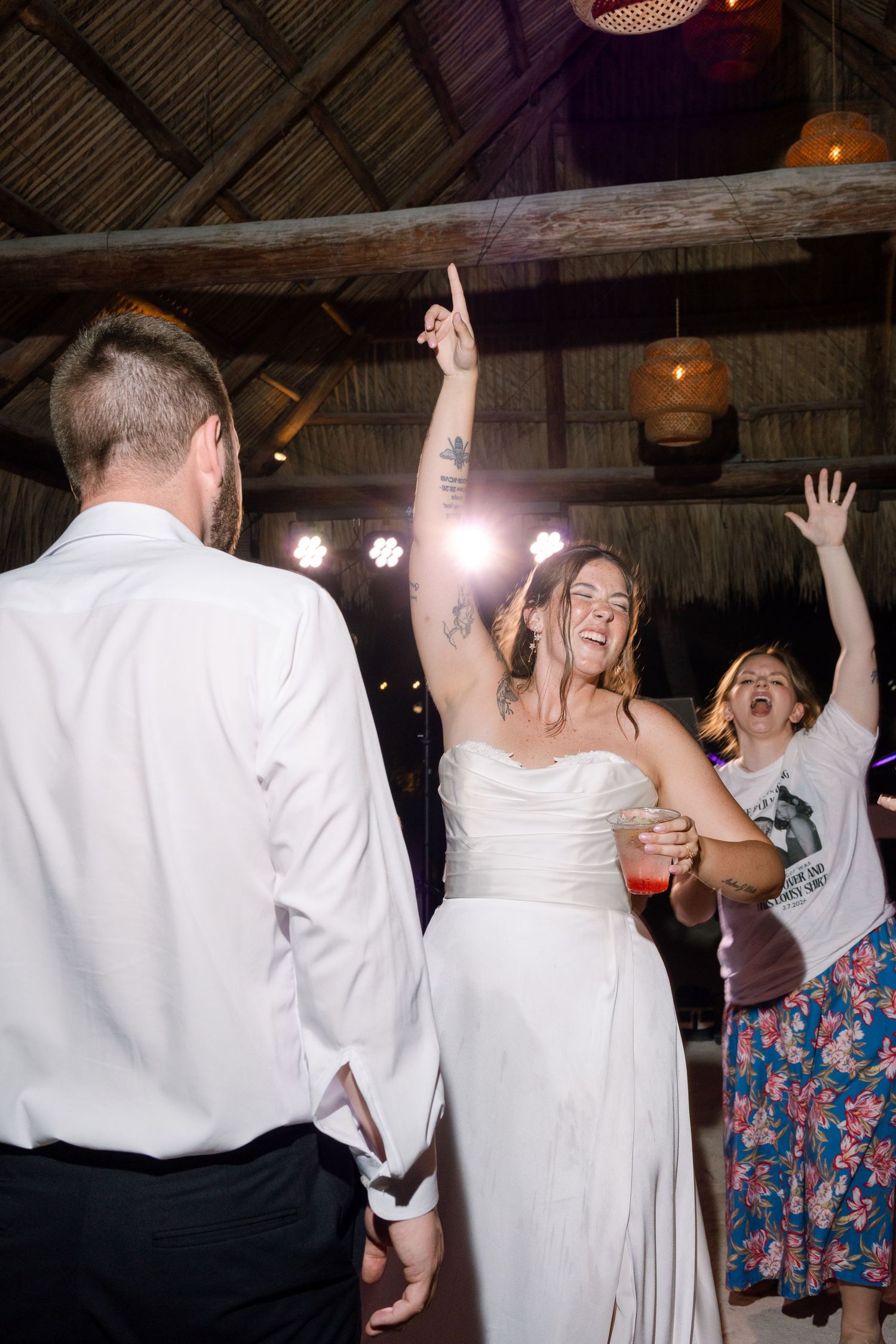 A bride and her guests are dancing and celebrating at a wedding reception in a rustic, wooden-beamed venue.