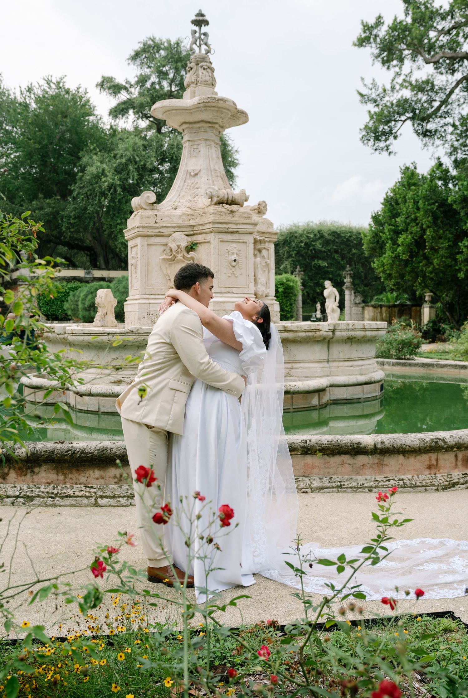 A romantic garden moment captured by an ornate stone fountain with red roses blooming in the foreground.