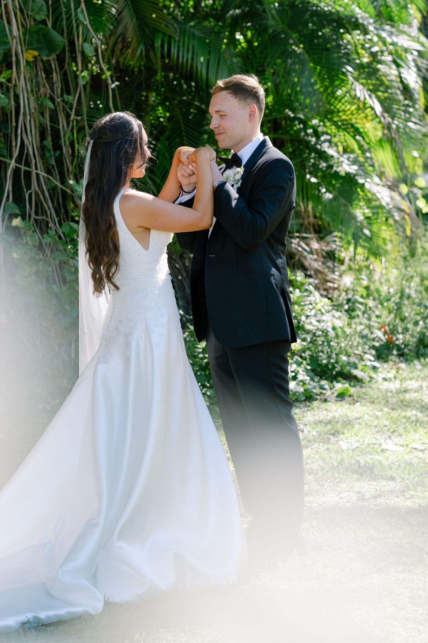 Bride and groom sharing first look moment, holding hands in lush tropical garden setting on wedding day.