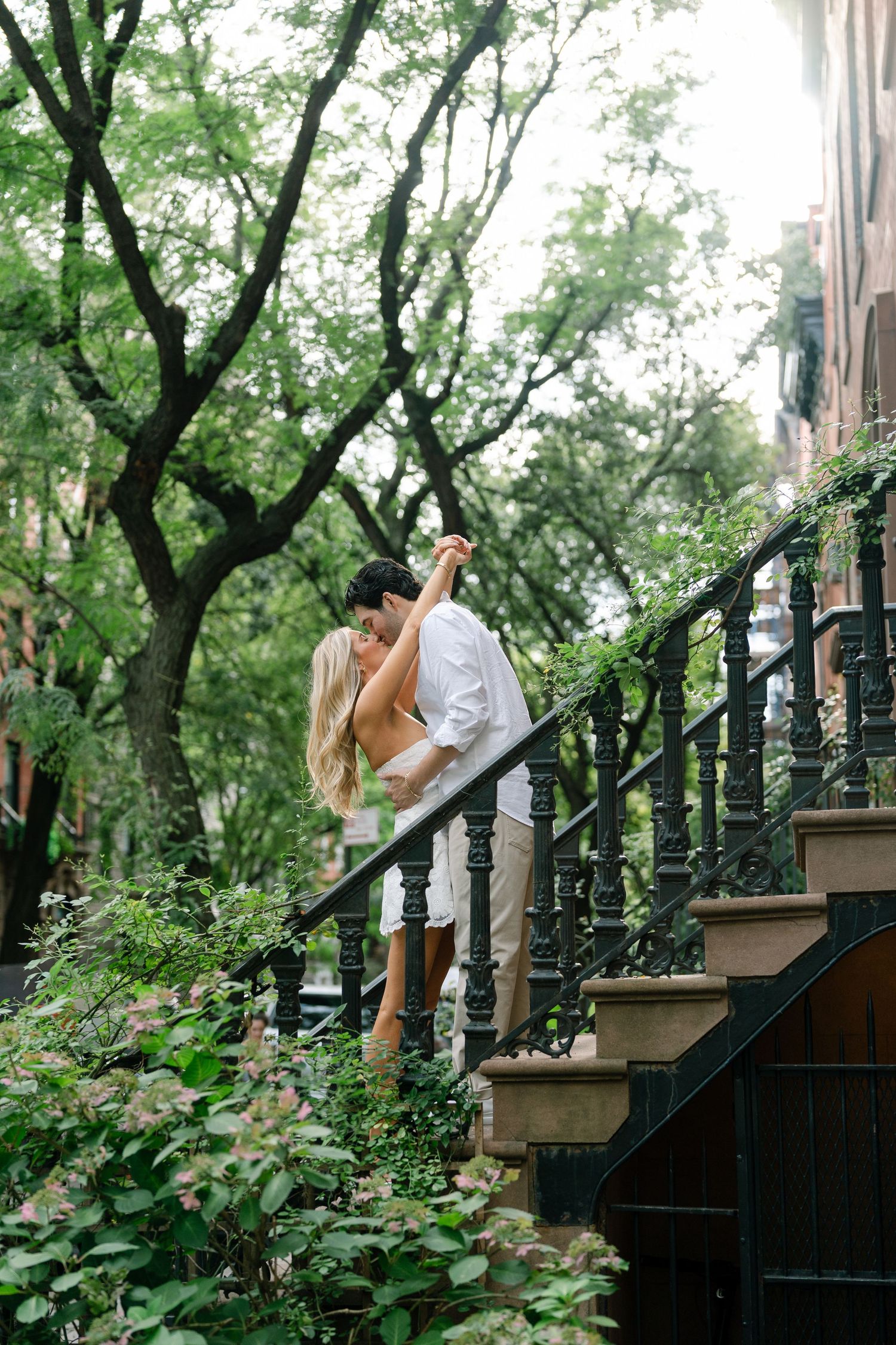Couple dancing romantically on iron staircase surrounded by lush green trees and foliage in an urban setting.