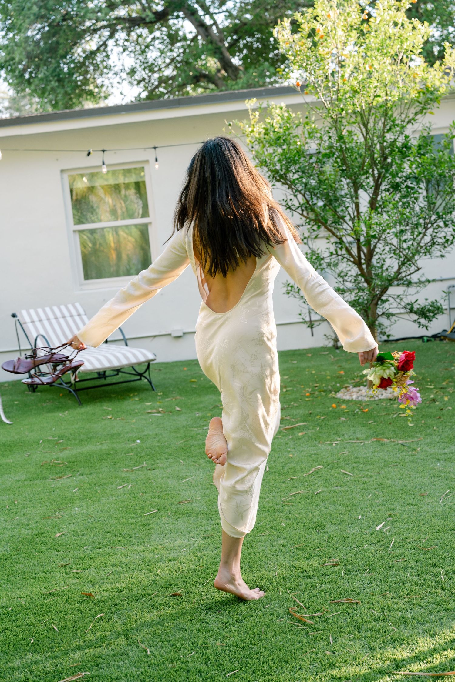 Someone in a flowing cream outfit dances and twirls on a sunlit green lawn.