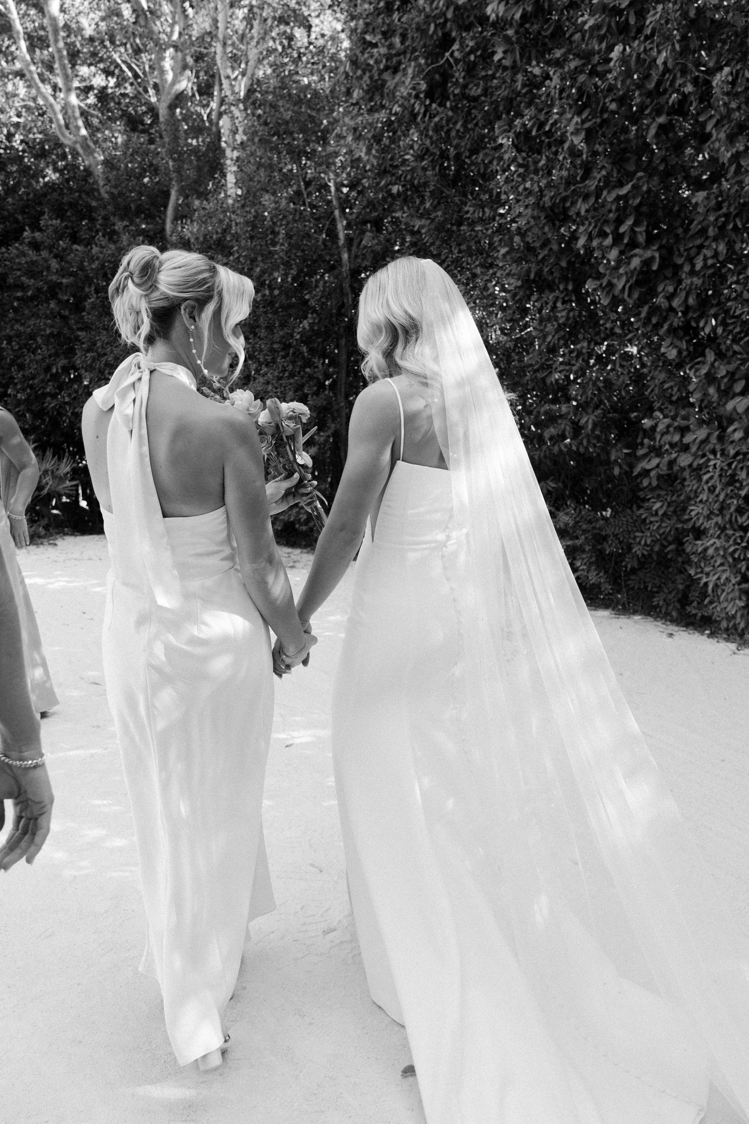 Wedding party walking in white dresses through a garden setting.