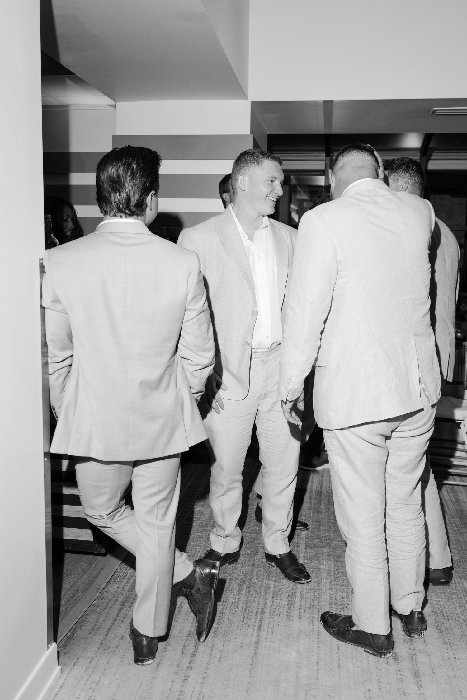 Black and white photo of groomsmen in light colored suits walking down a hallway.