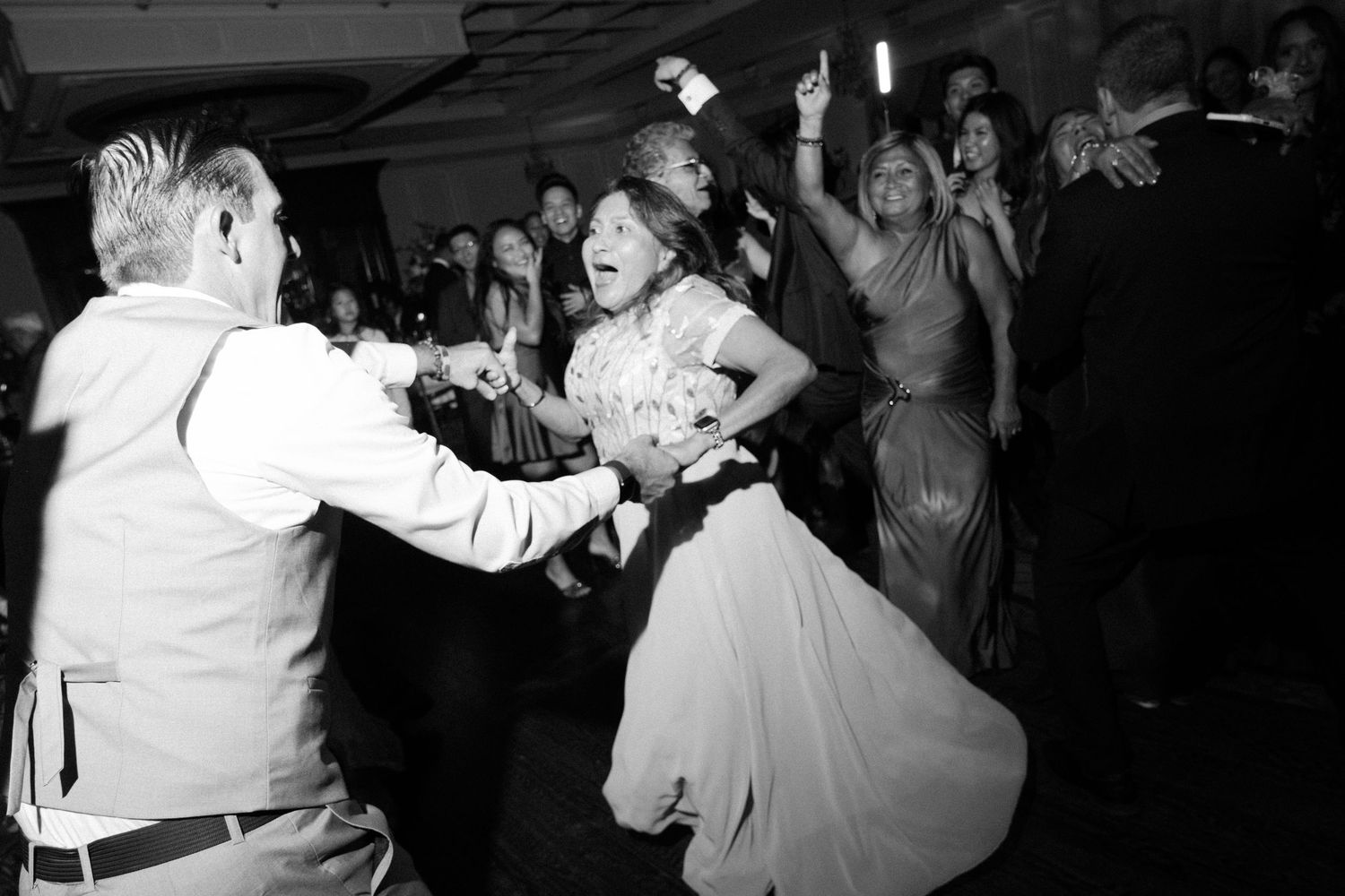 Wedding guests dancing energetically in black and white on a lively dance floor.