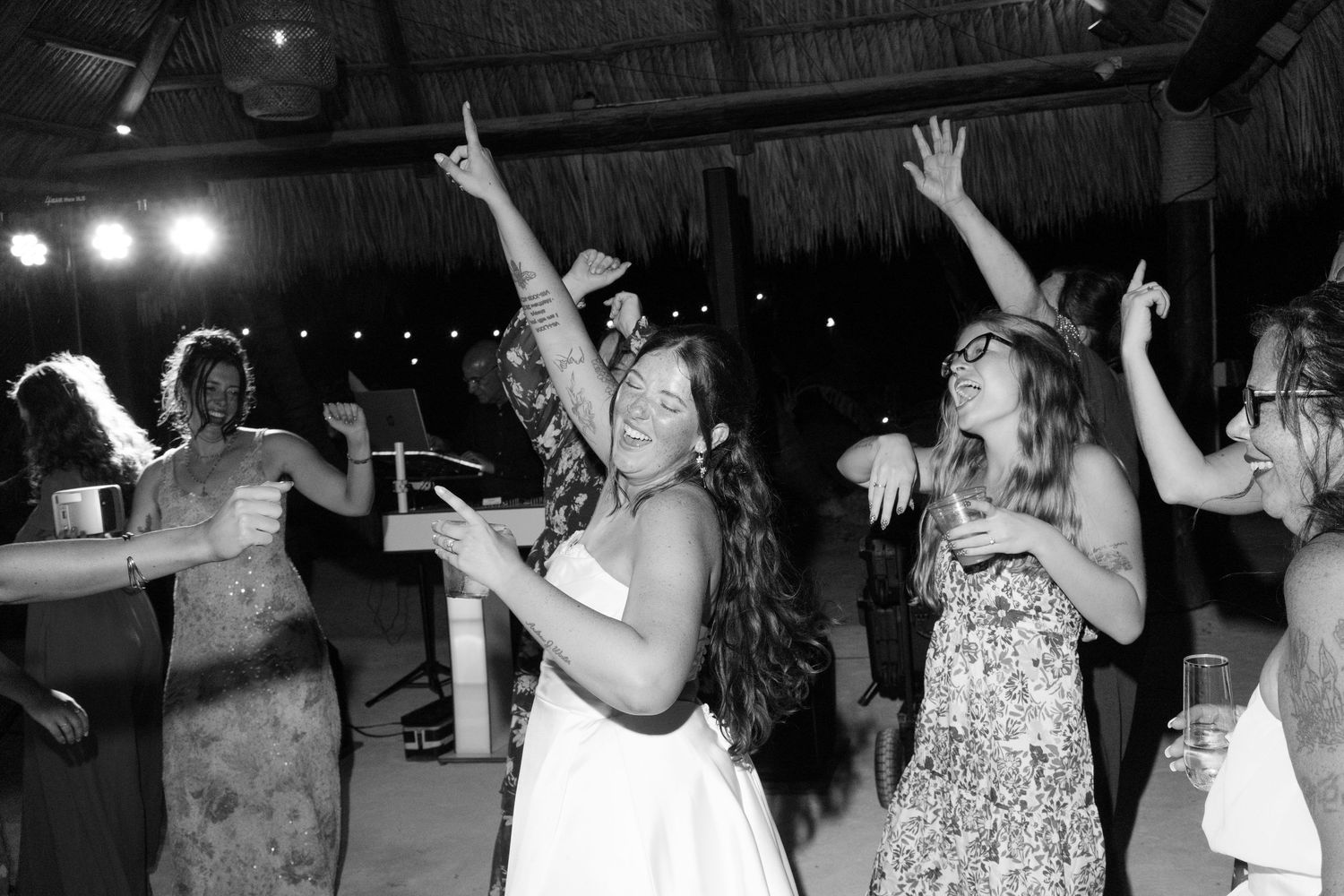A black and white image of people dancing at a party or event, with a woman in the center raising her arms.
