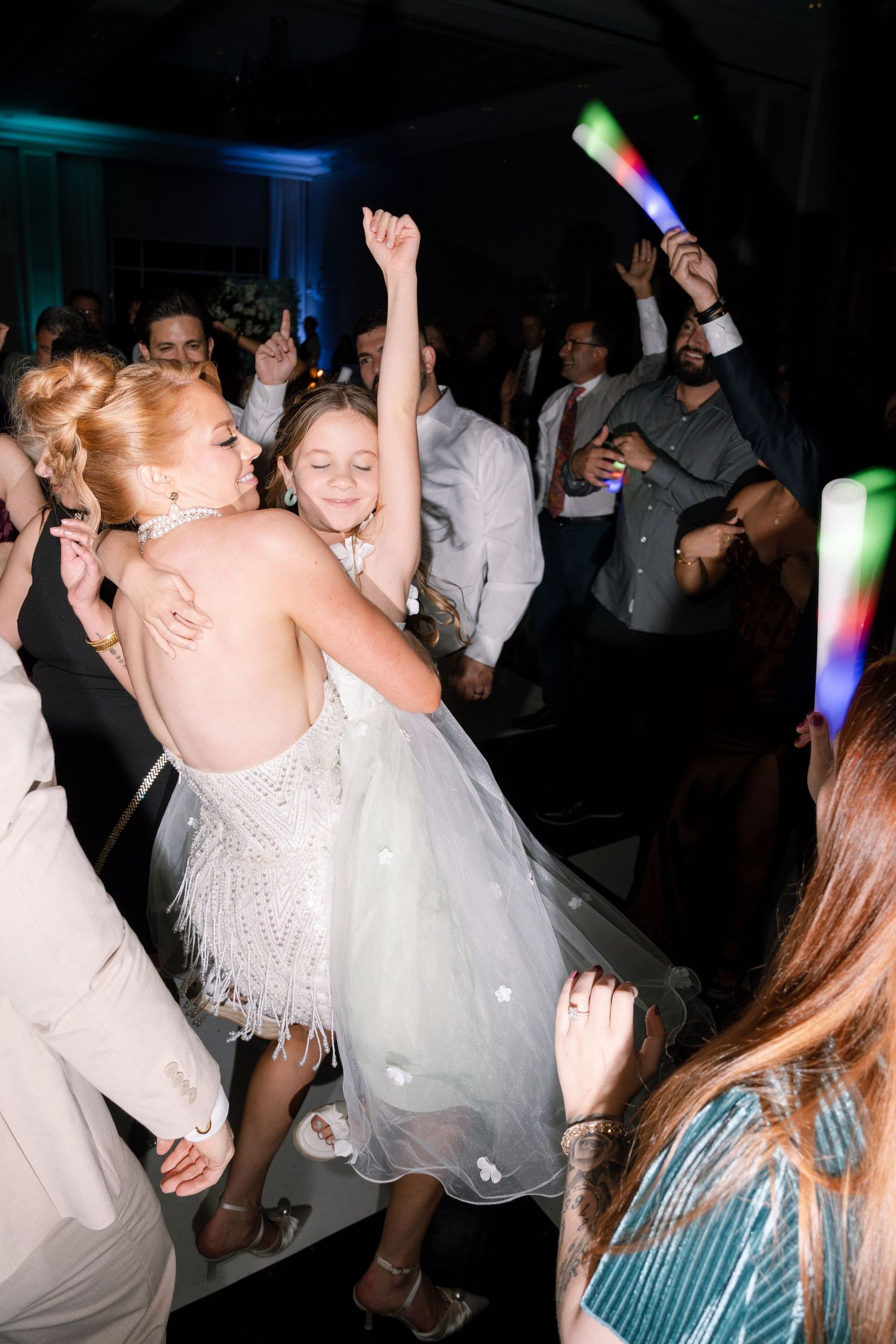 Wedding reception dance party with glowing light sticks and guests in white attire.