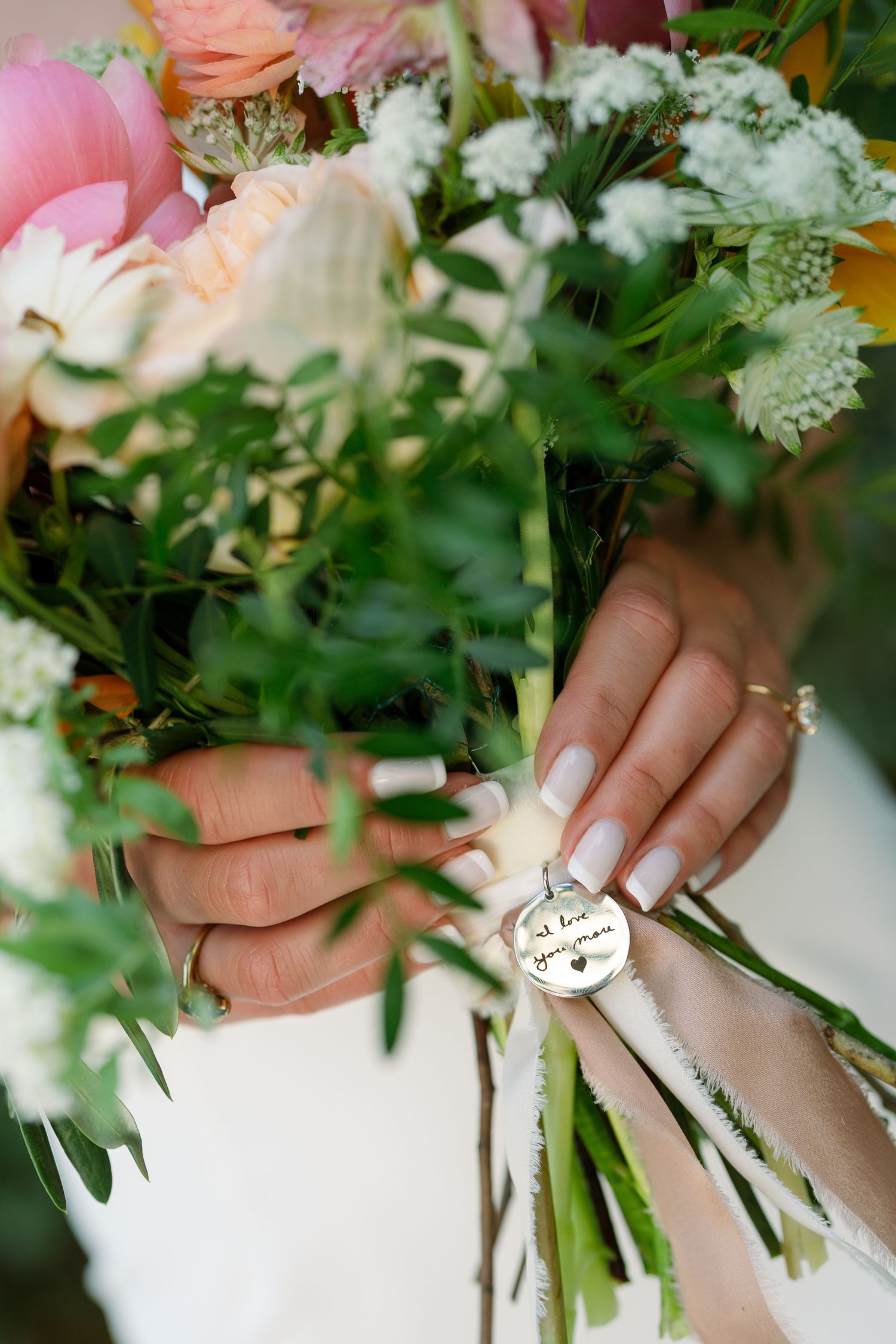 Hands holding a bridal bouquet with pink and white flowers against a soft background.