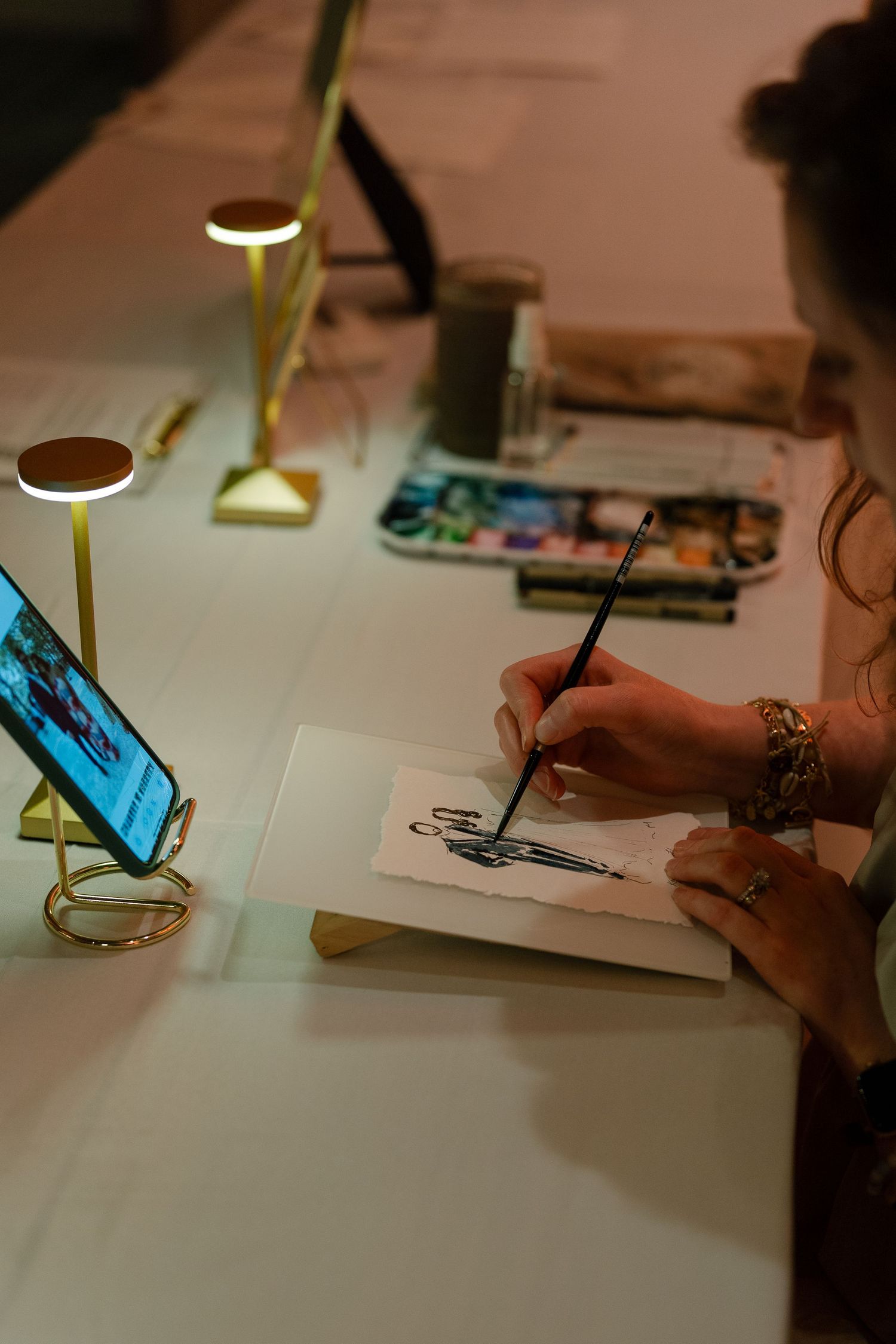 Close-up of hands drawing or writing at desk with task lamp.