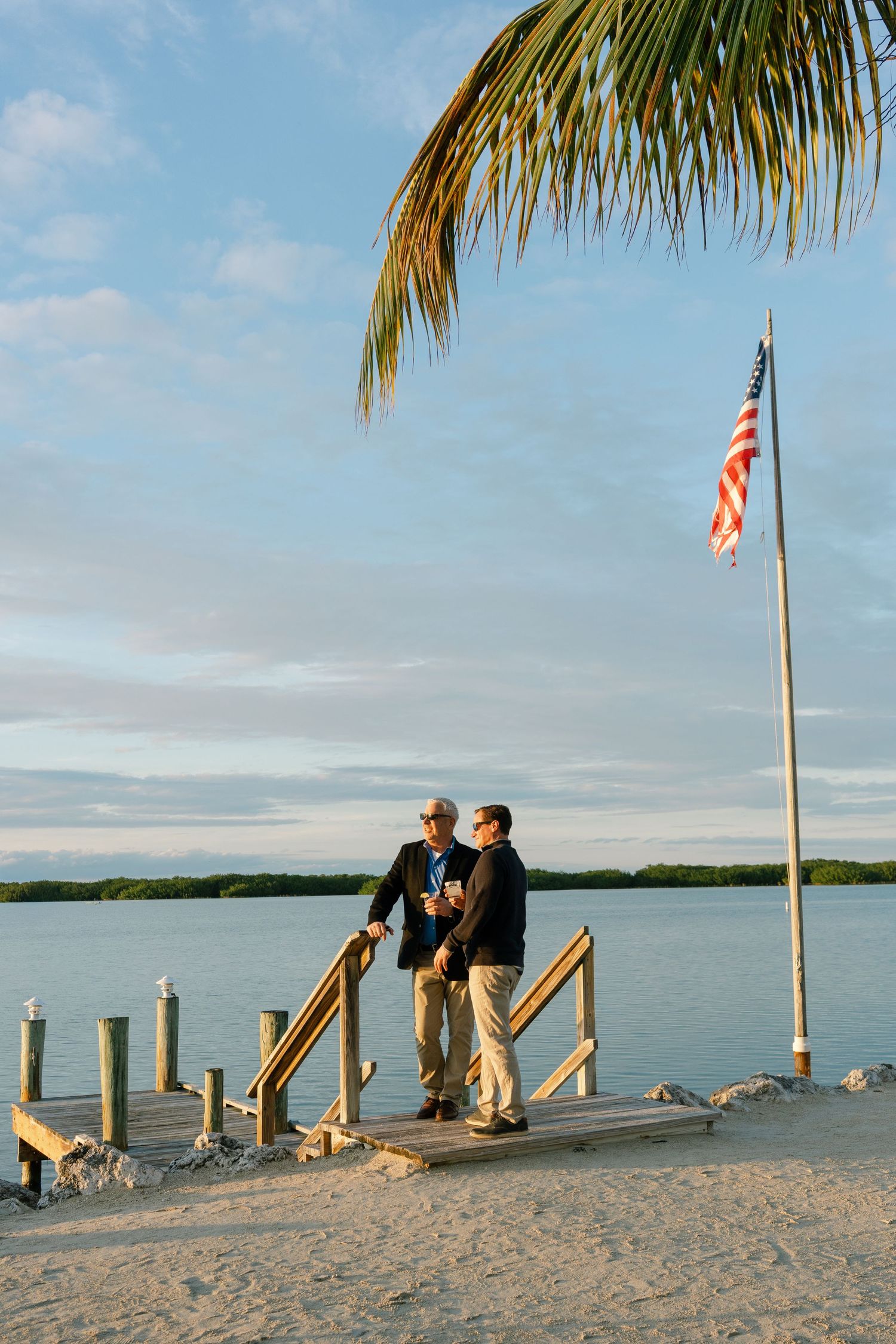 Scenic waterfront dock with American flag and palm fronds at sunset.