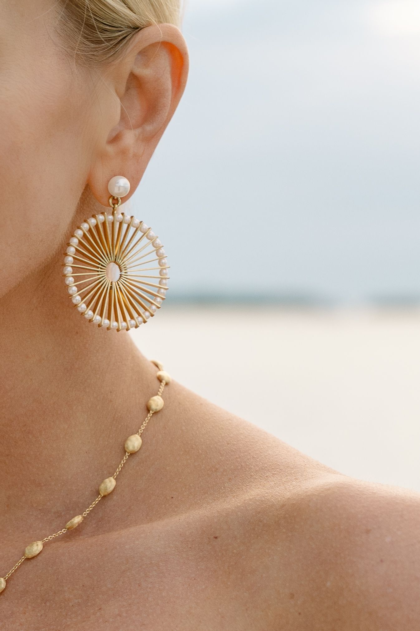 Gold sunburst fan-shaped statement earring with pearl accents shown in a close-up profile view against a soft background.