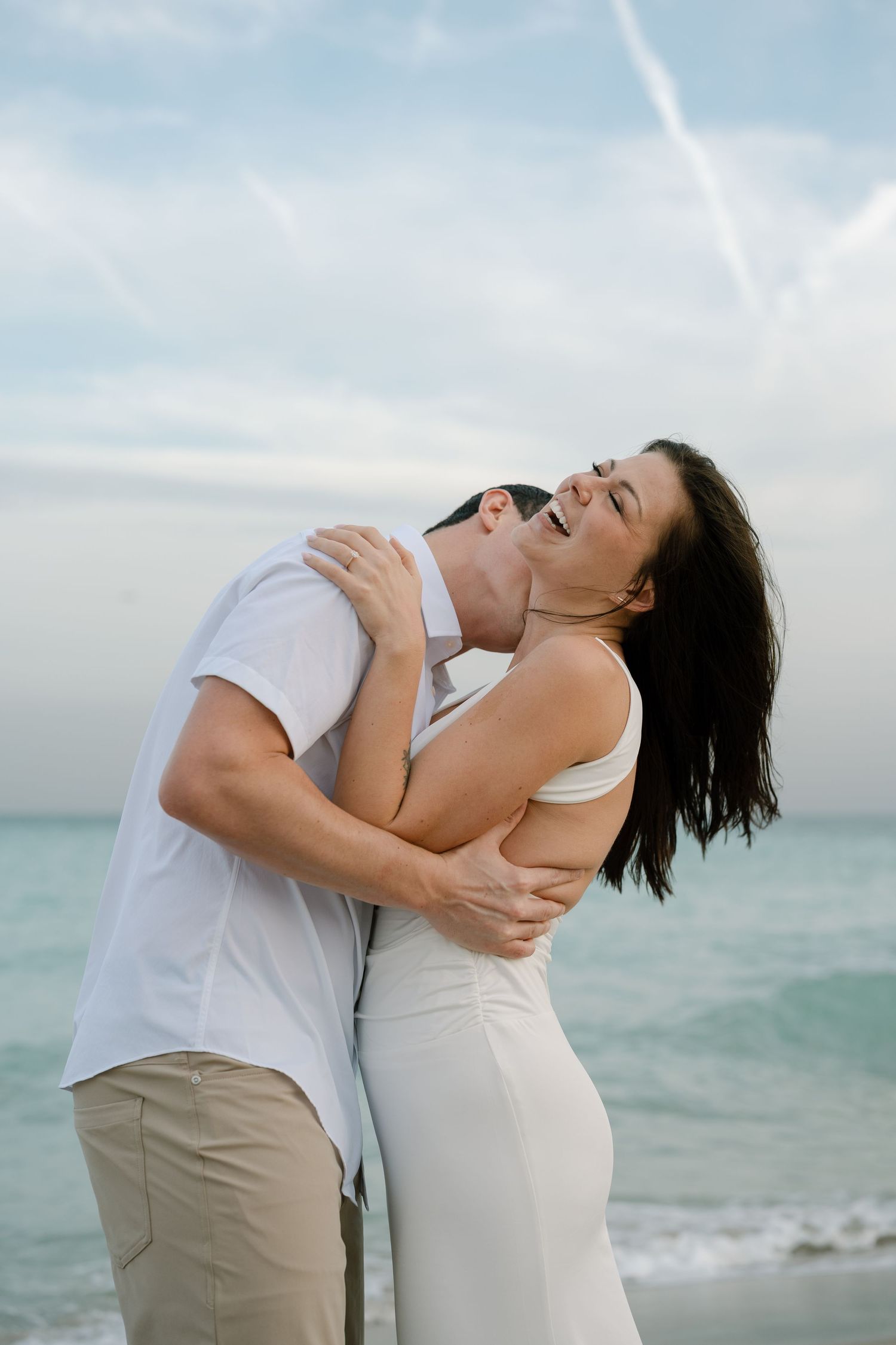 Joyful couple laughing and embracing by the turquoise ocean.