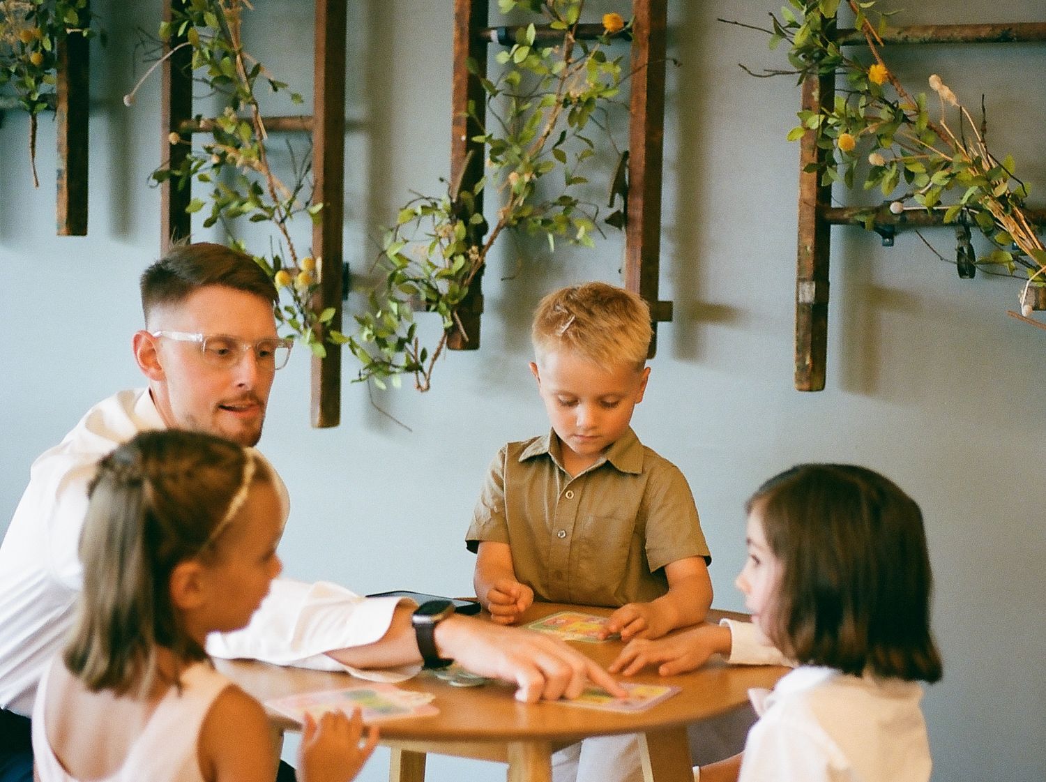 People gathered around wooden tables decorated with greenery for a casual indoor celebration.