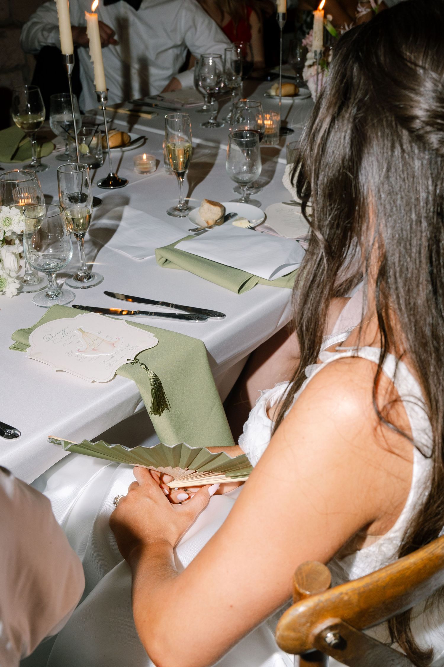 Bride reading menu card at elegantly set wedding reception table with candles, sage napkins, and glassware.