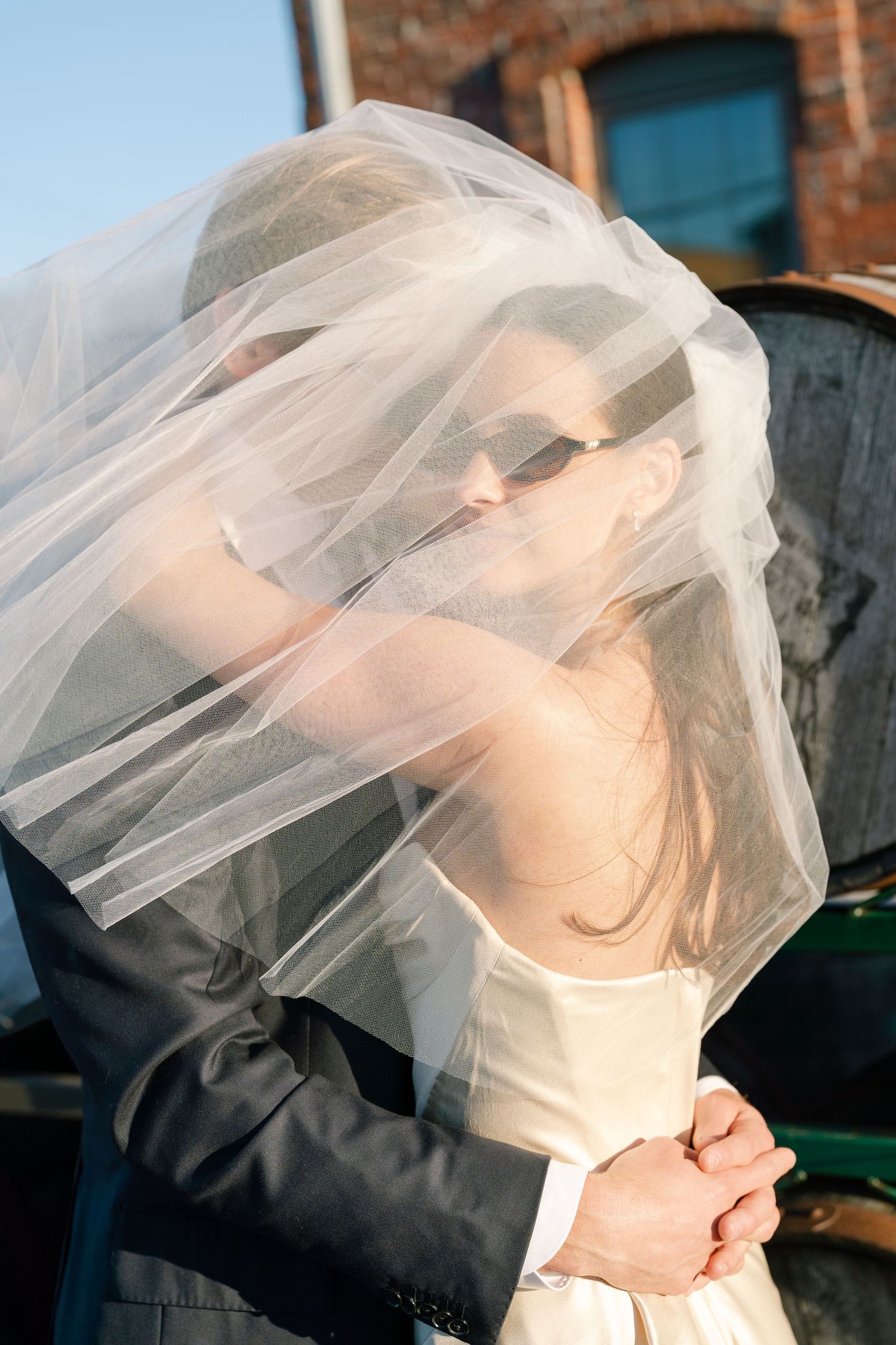 Bride and groom sharing an intimate moment under a flowing white veil at an outdoor wedding.
