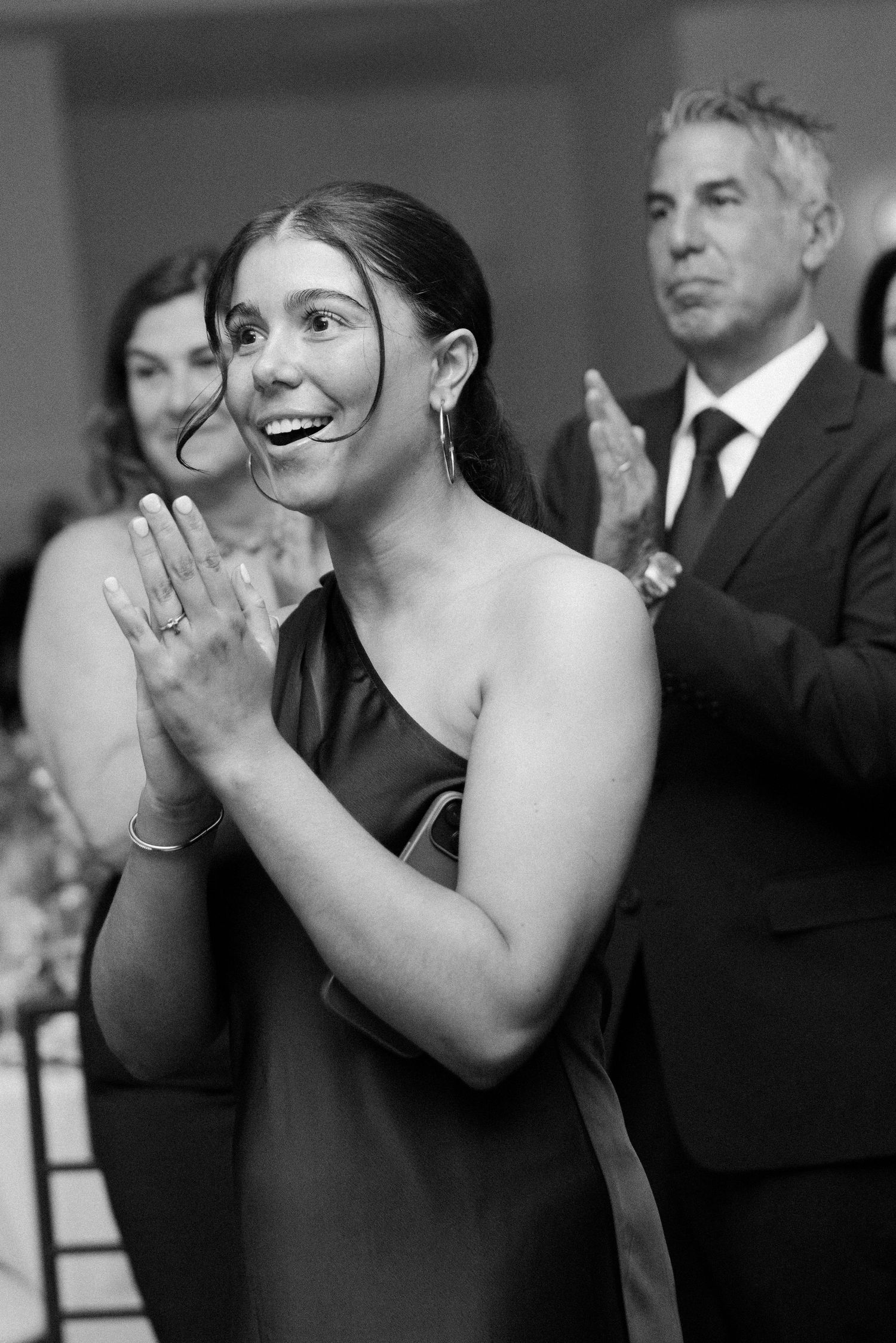 Black and white candid photo of wedding guests clapping and celebrating during reception.