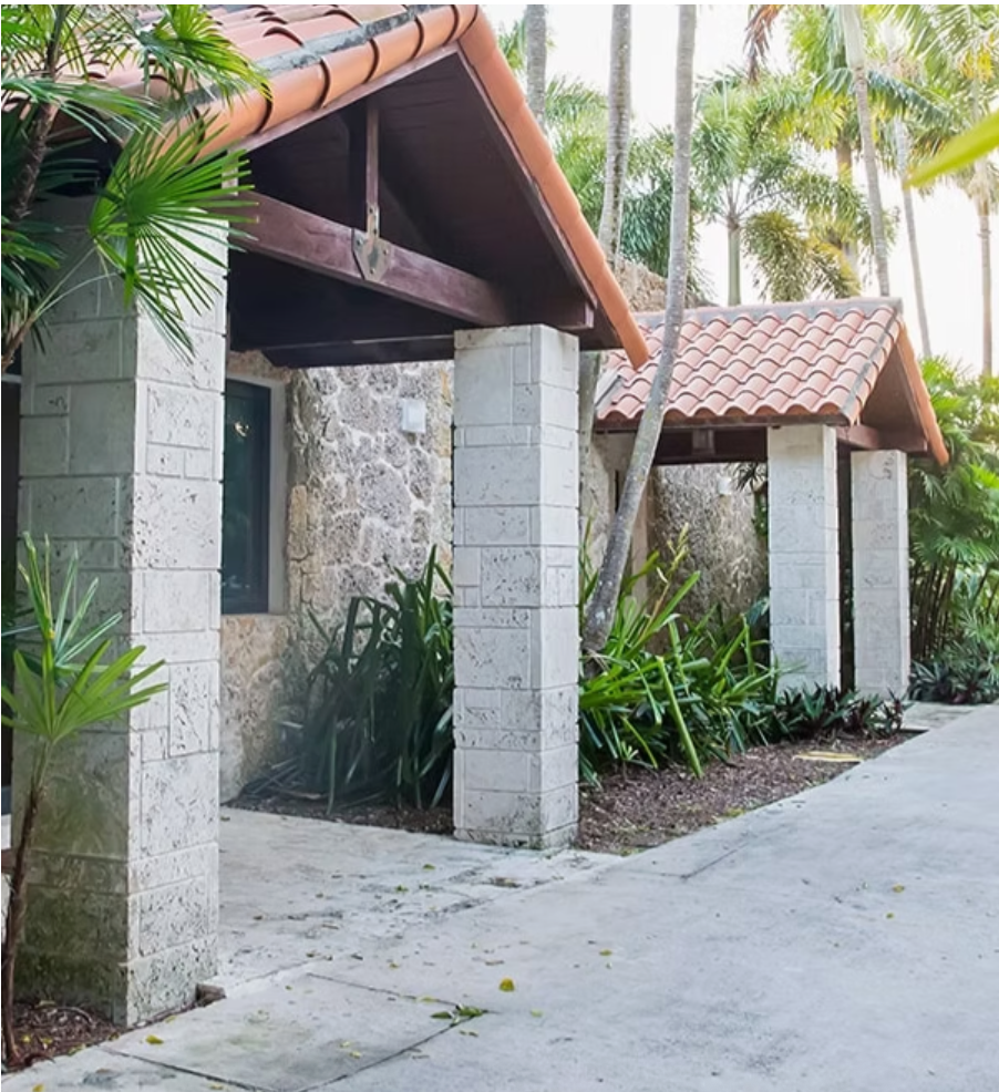 Stone and terracotta outdoor restroom building with palm trees and tropical landscaping at a resort facility.