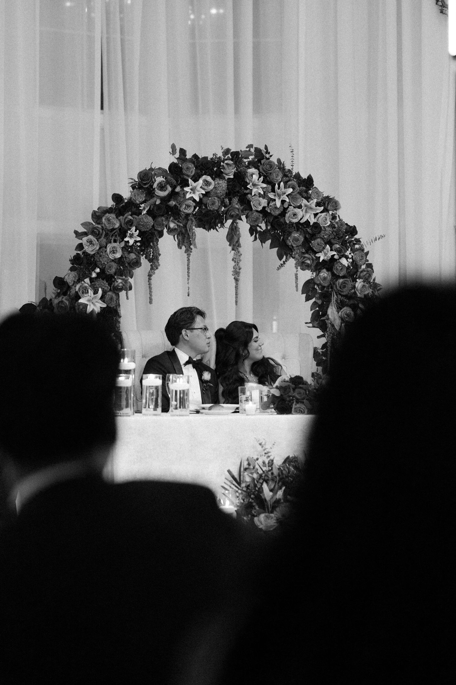 Black and white panoramic view of an elegant wedding reception with floral decorations on the head table.
