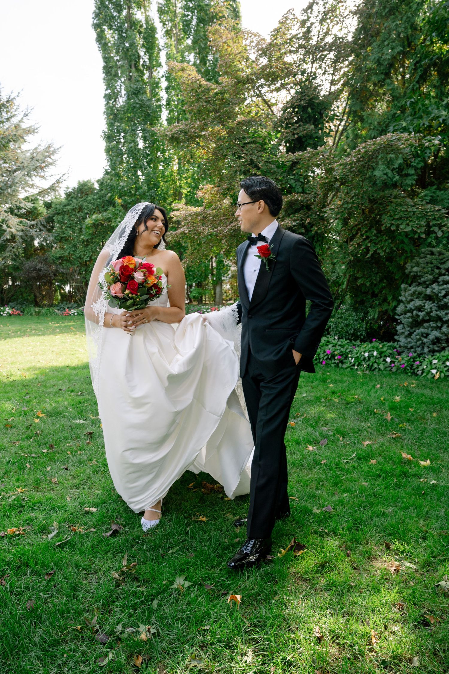 Playful outdoor wedding portraits with bride in flowing white dress and groom in classic black tuxedo.