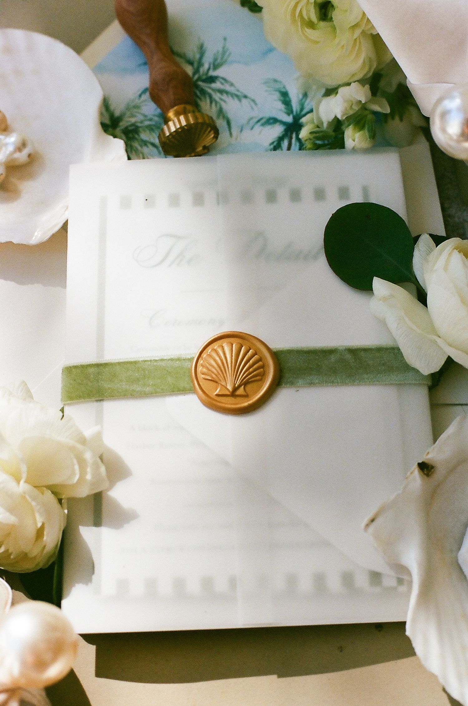 Elegant wedding stationery with white flowers and a gold wax seal displayed on a soft surface.