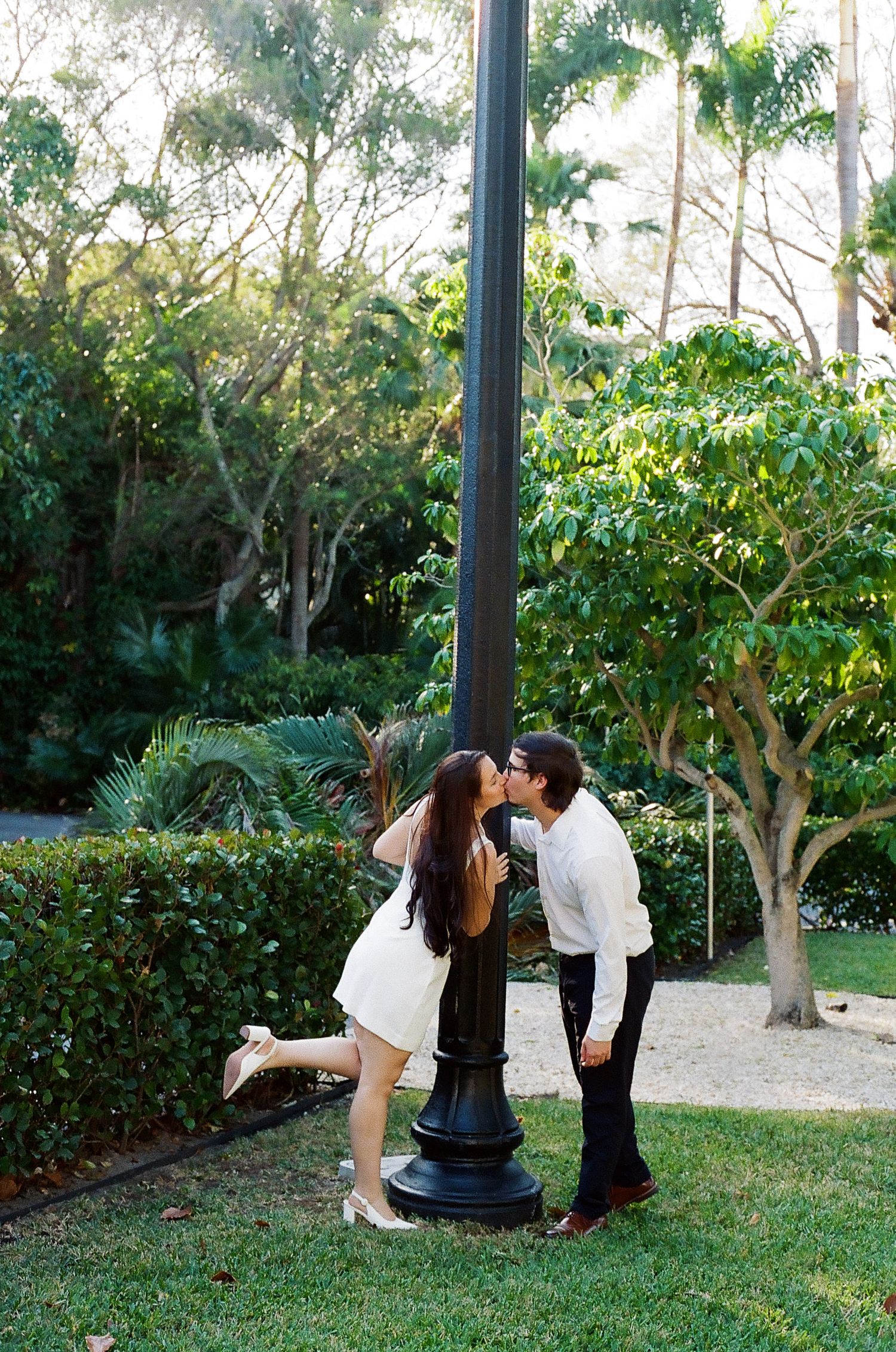A romantic scene unfolds as a couple shares an intimate moment near a lamp post in a garden setting.