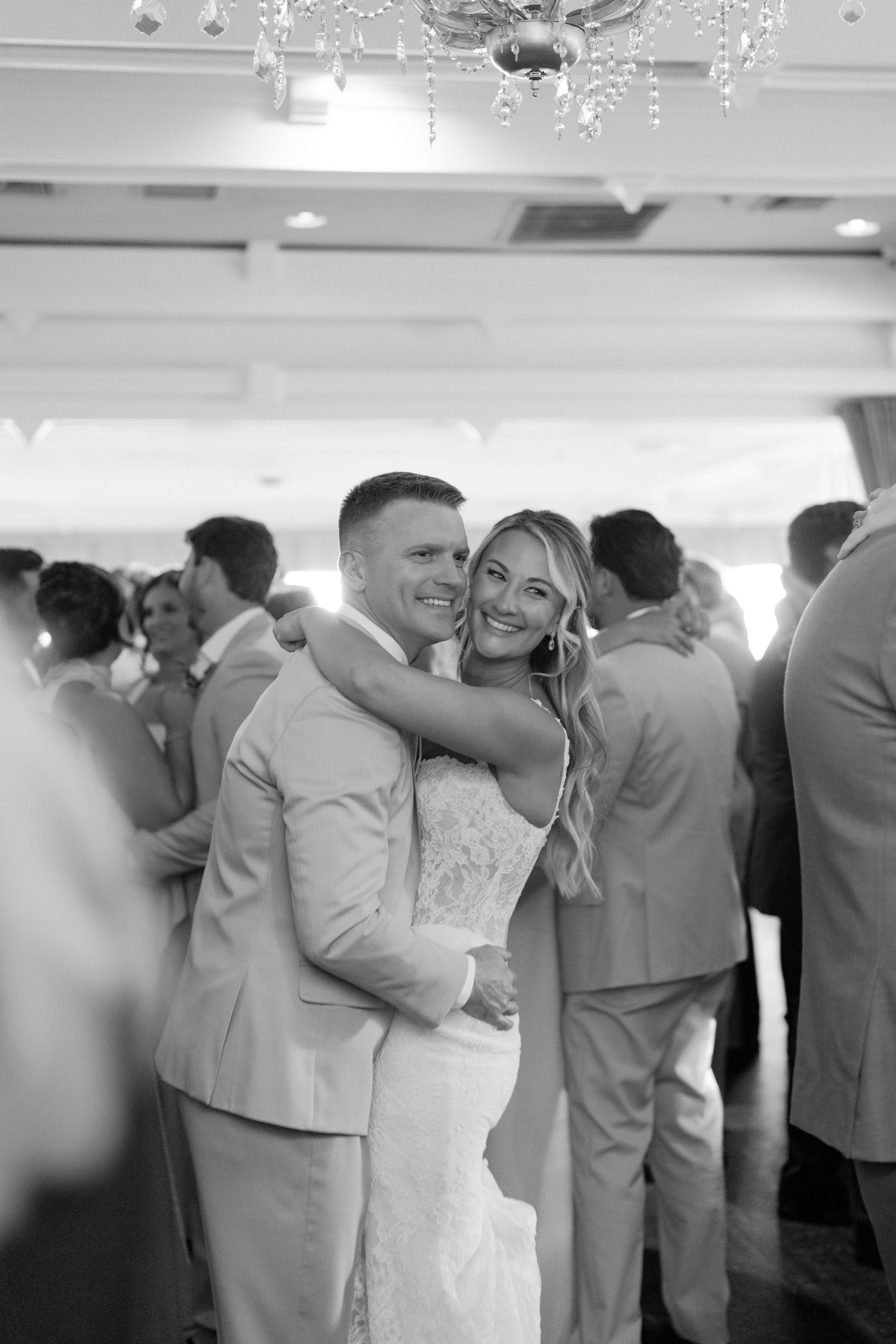 Black and white photo of smiling bride and groom embracing on dance floor at elegant wedding reception.