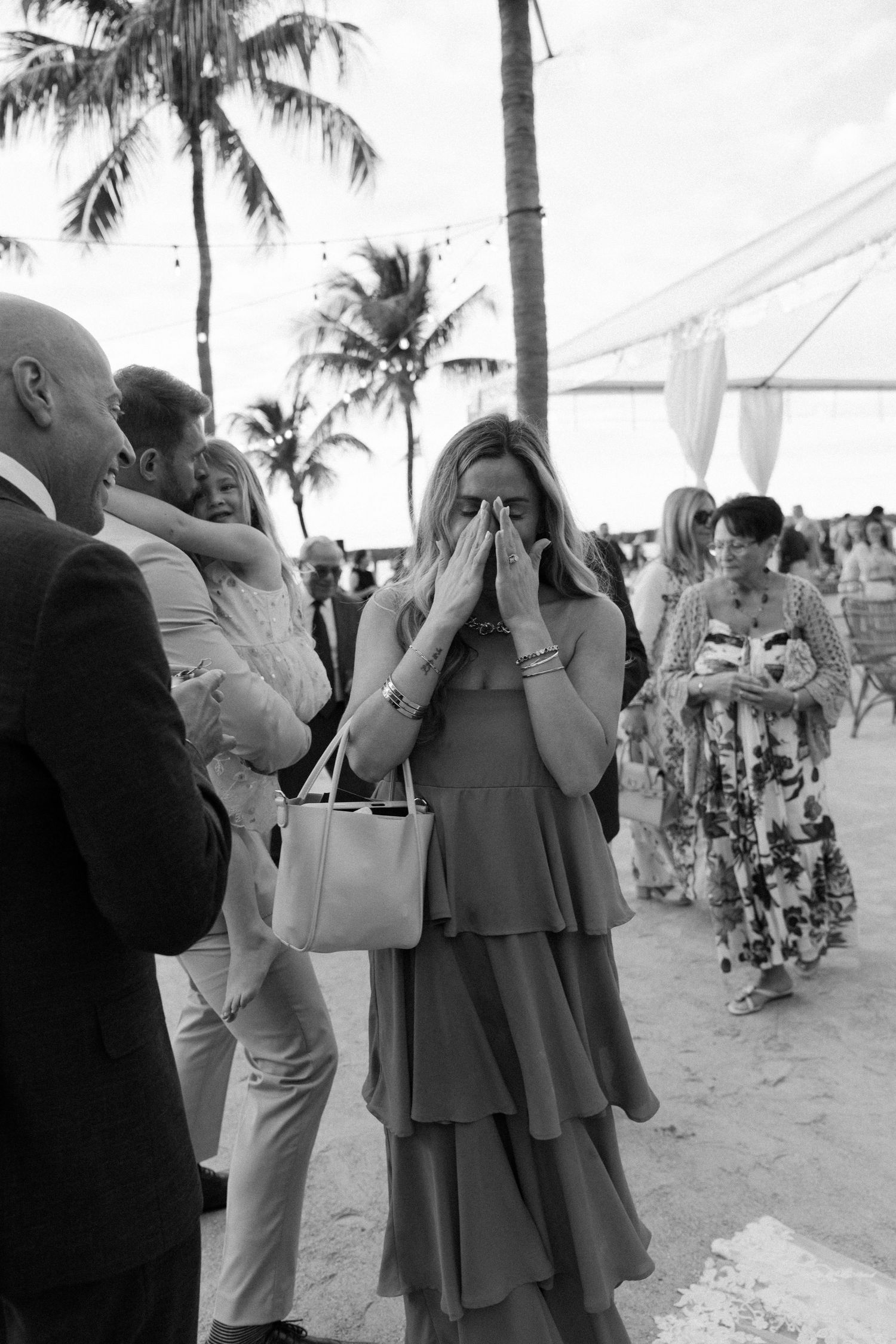 Black and white photo of wedding guests at a tropical beach reception with palm trees.