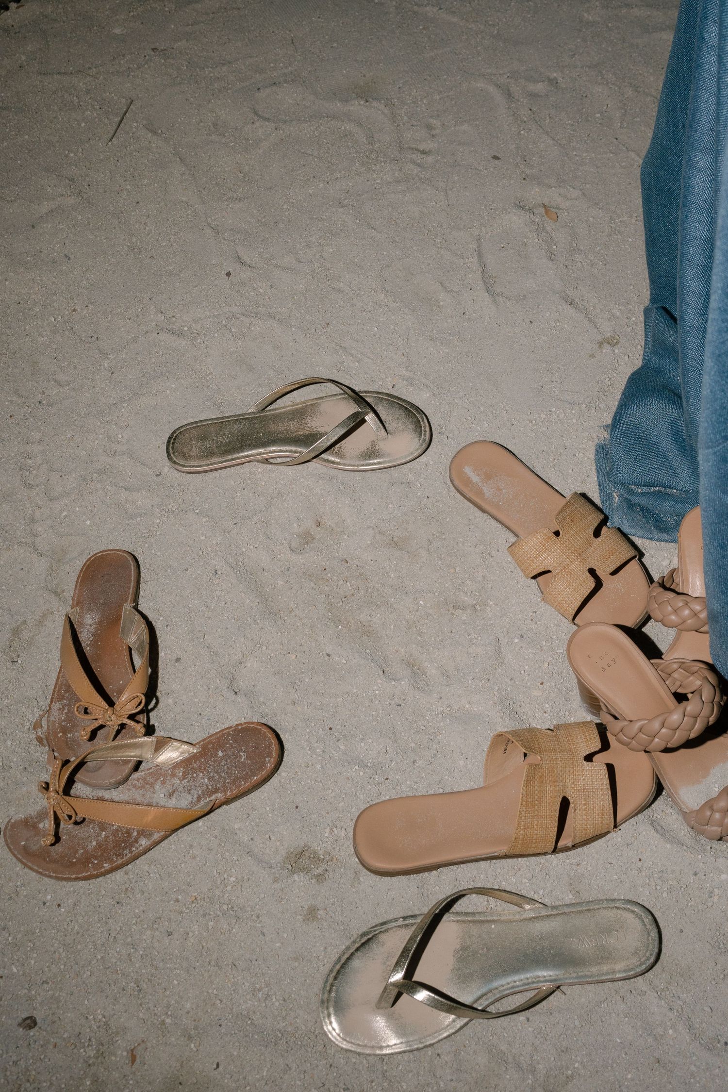 Various beach sandals and flip flops scattered on sandy ground at a coastal event.