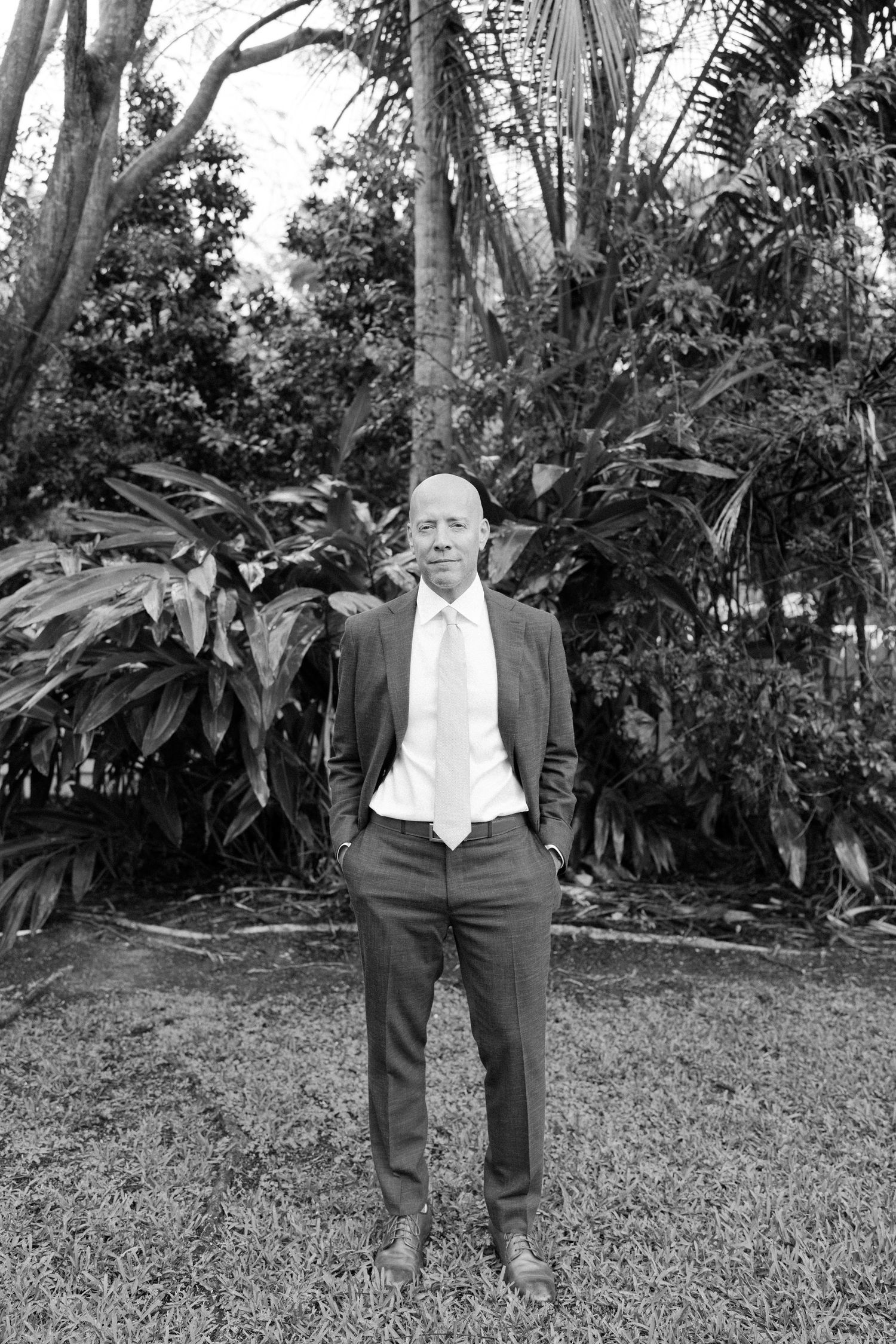 Wedding party members in formal attire pose in a tropical garden setting.