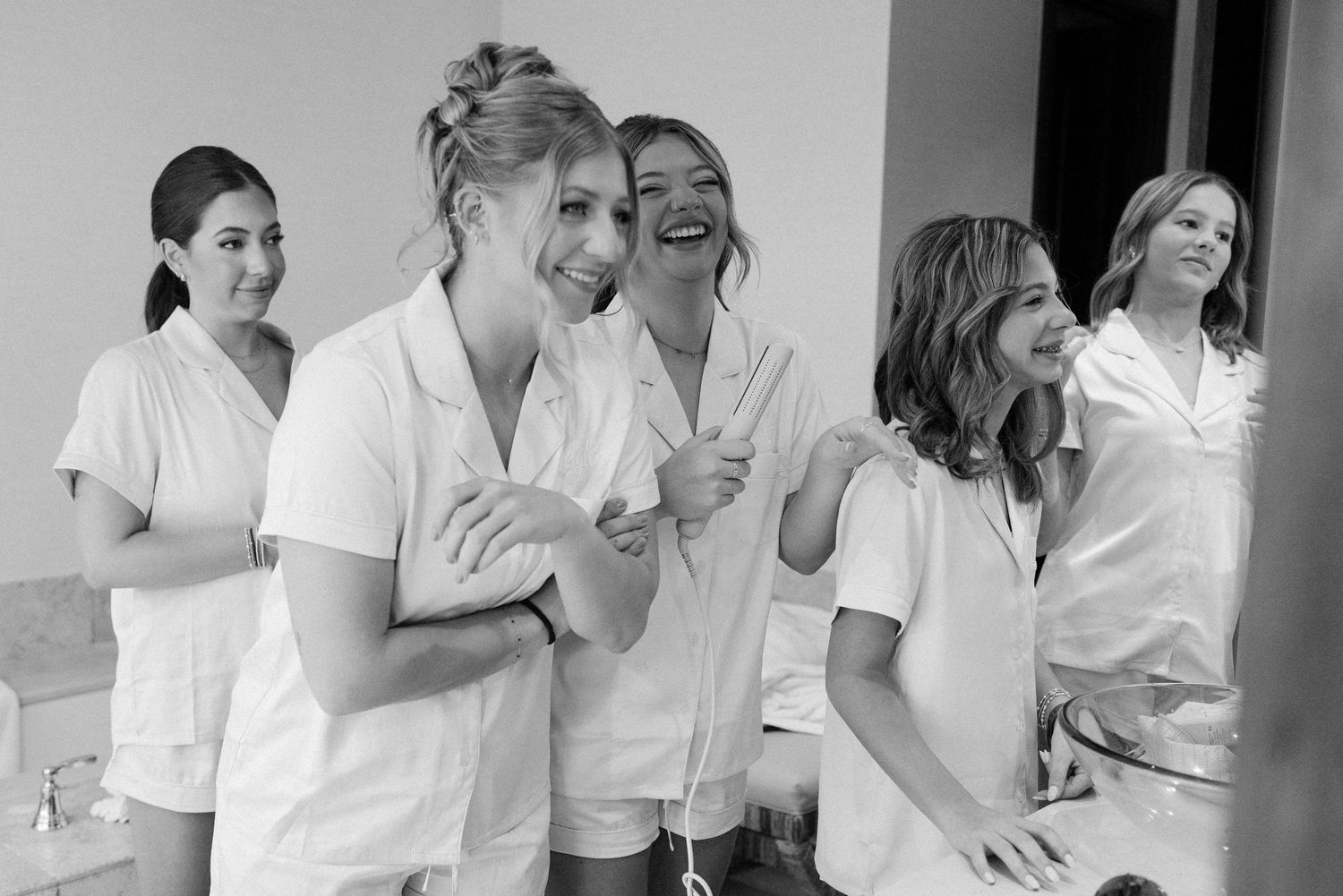 Group of people in white shirts laughing and embracing in a casual indoor setting.