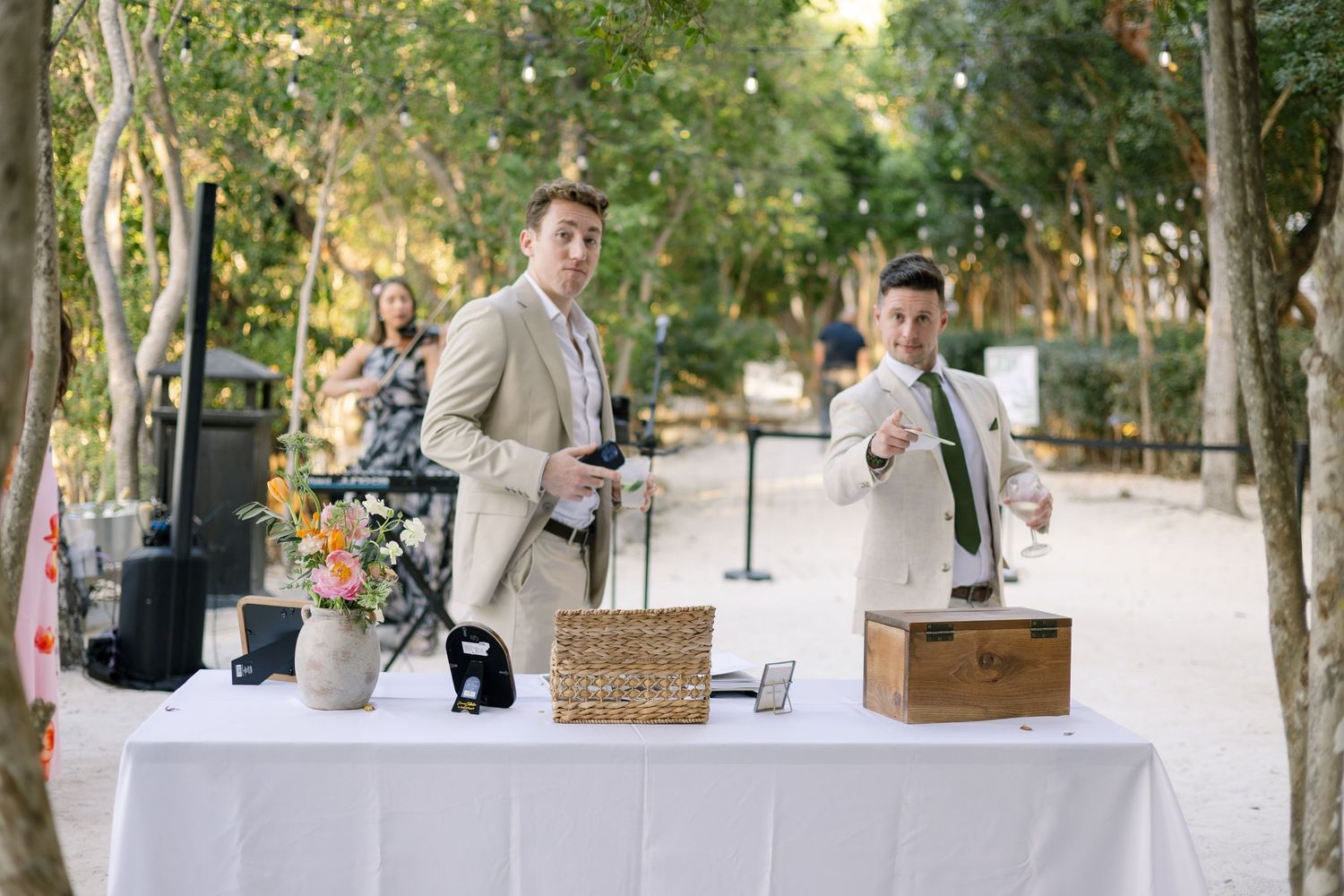 Outdoor wedding reception setup with tables and decor under trees.