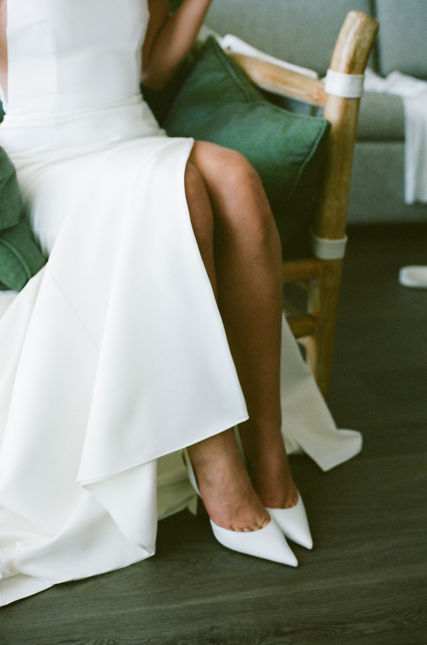 Detail shot of white wedding dress hem and shoes against dark flooring.