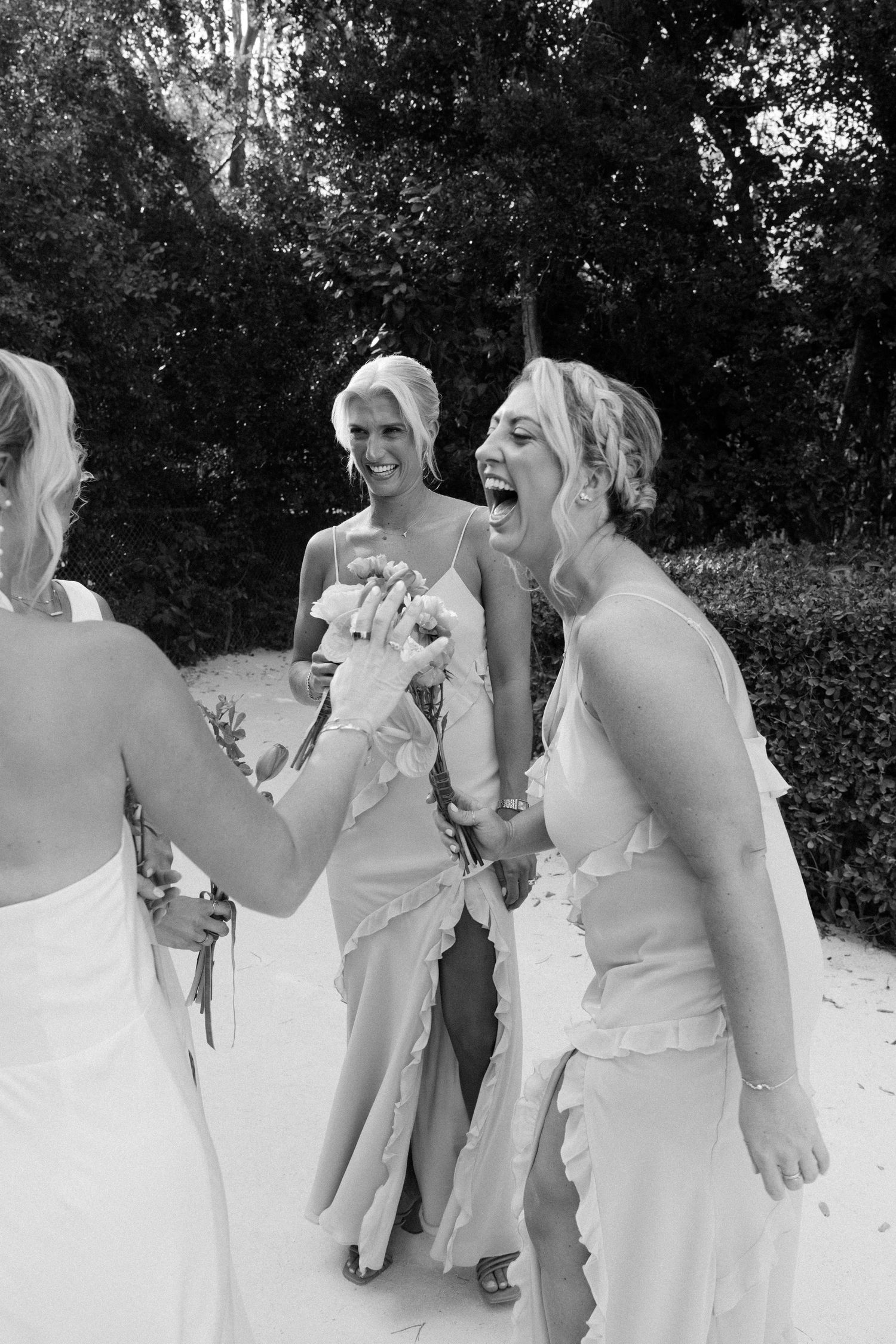 A candid black and white photo of bridesmaids in white dresses sharing a joyful moment outdoors.