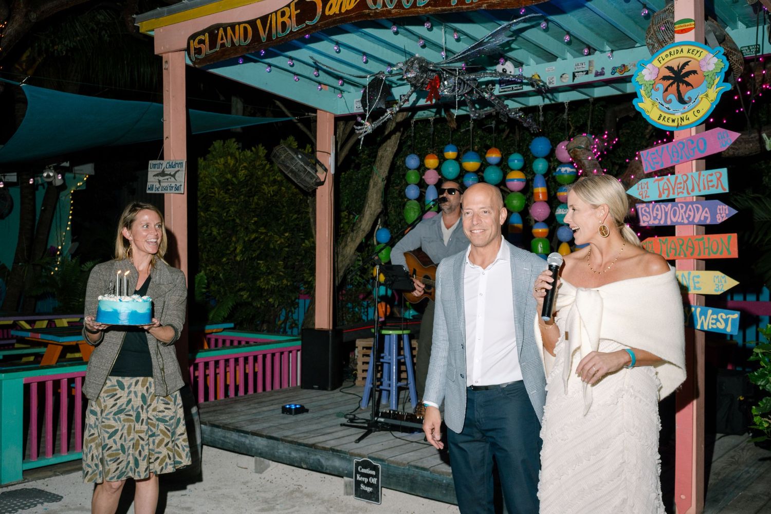 People enjoying a festive evening at a tropical-themed venue with colorful lights and decorative elements.