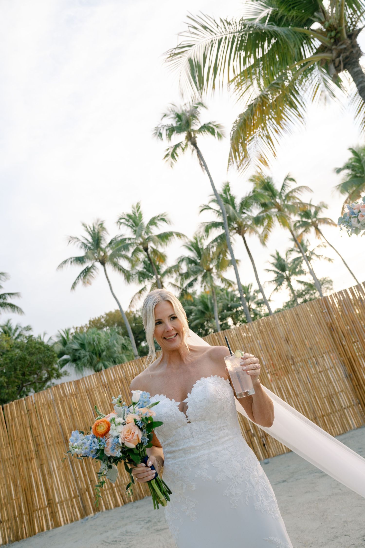 Beachside wedding photography with palm trees and bamboo fence in the background.