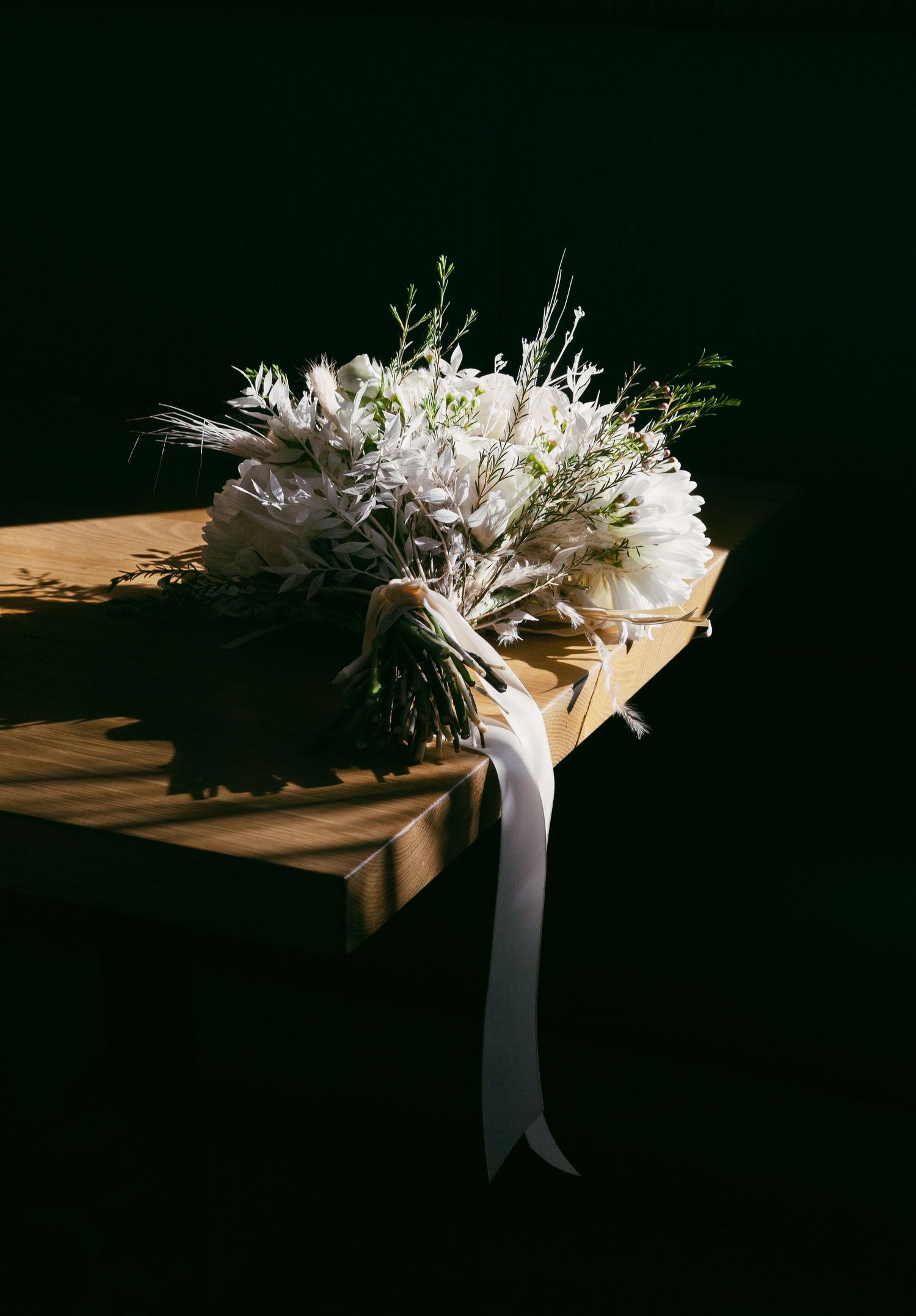 A dramatic sequence of a white bridal bouquet in low-key lighting casting long shadows on a wooden surface.