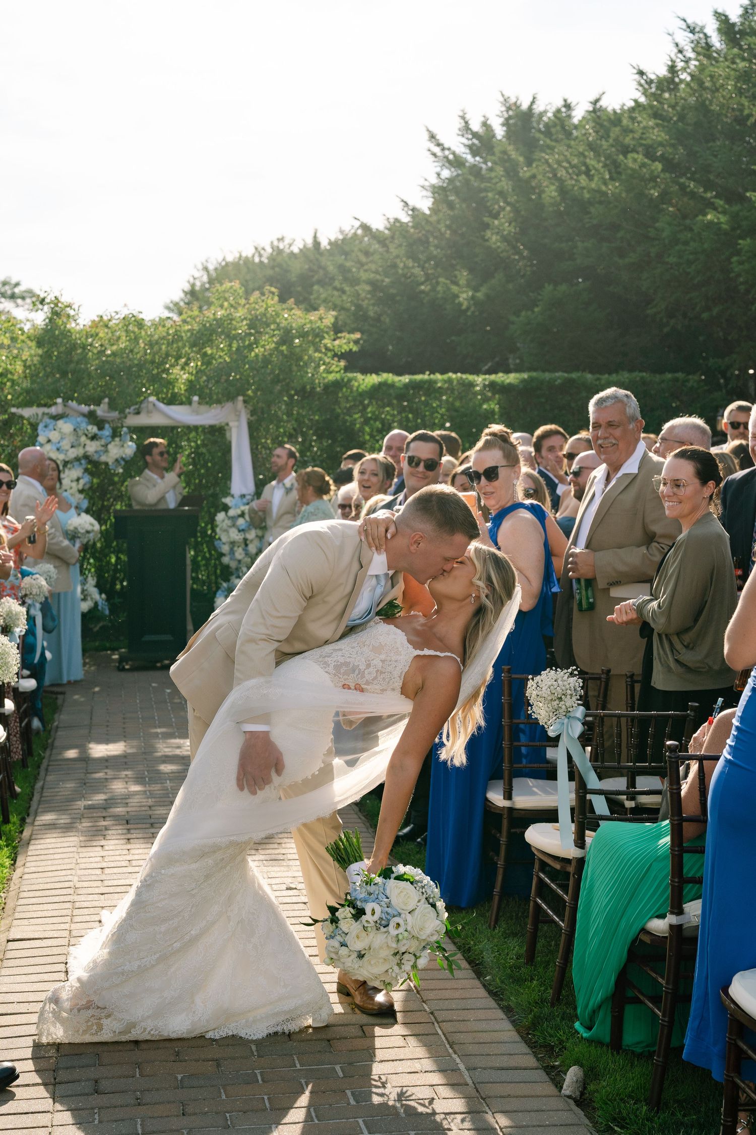 Bride and groom share a romantic dip kiss while walking down the aisle at outdoor wedding.