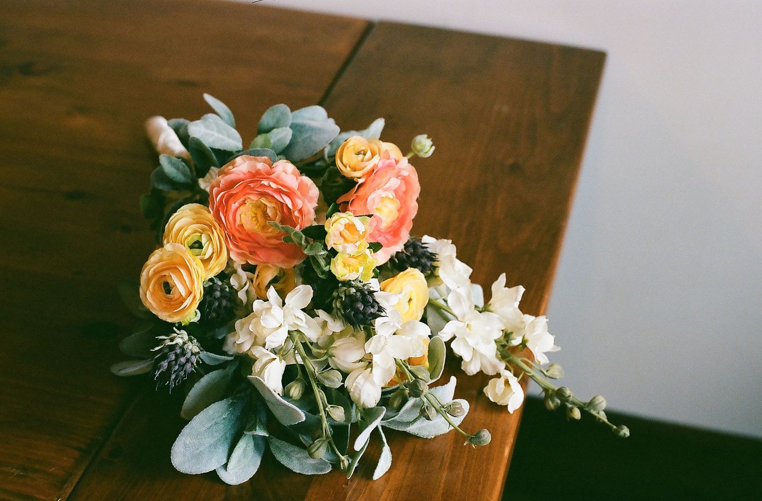 Beautiful floral arrangement featuring peach ranunculus and white flowers on a dark wooden surface.