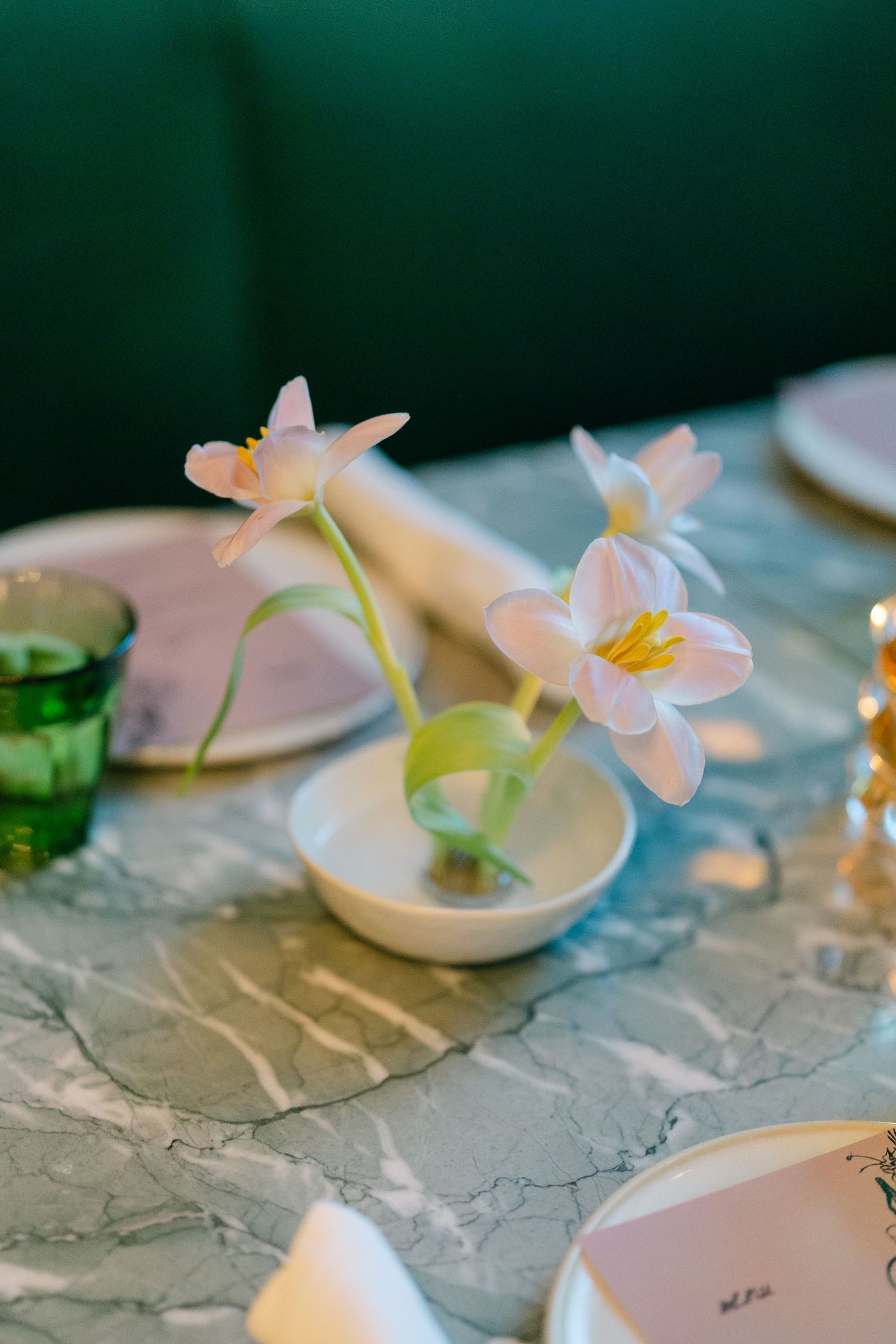 Delicate pink flowers arranged in small white bowls on a textured tablecloth.