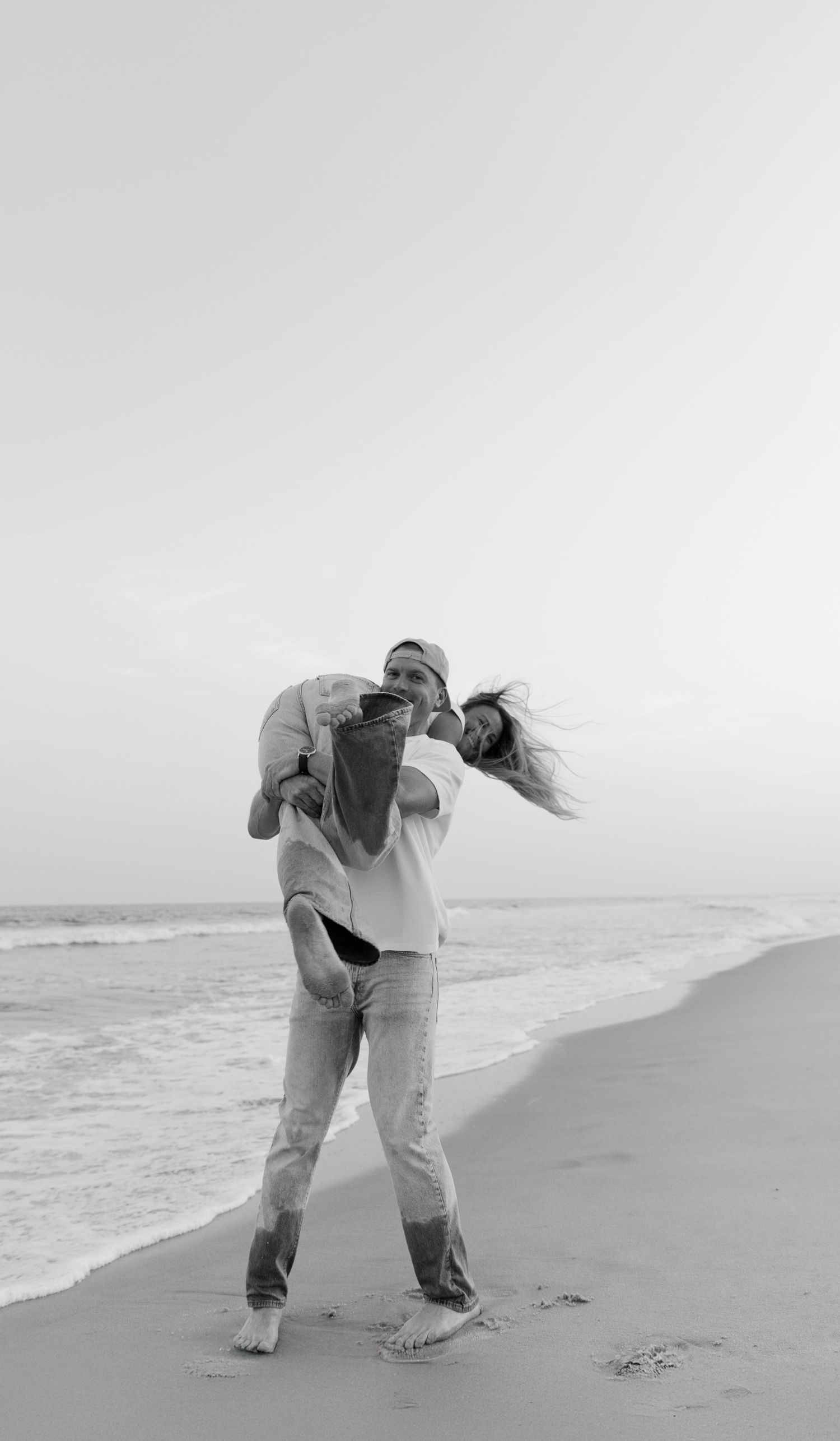 Black and white sequence of a person bending down to pick up sand on a beach with ocean waves in the background.