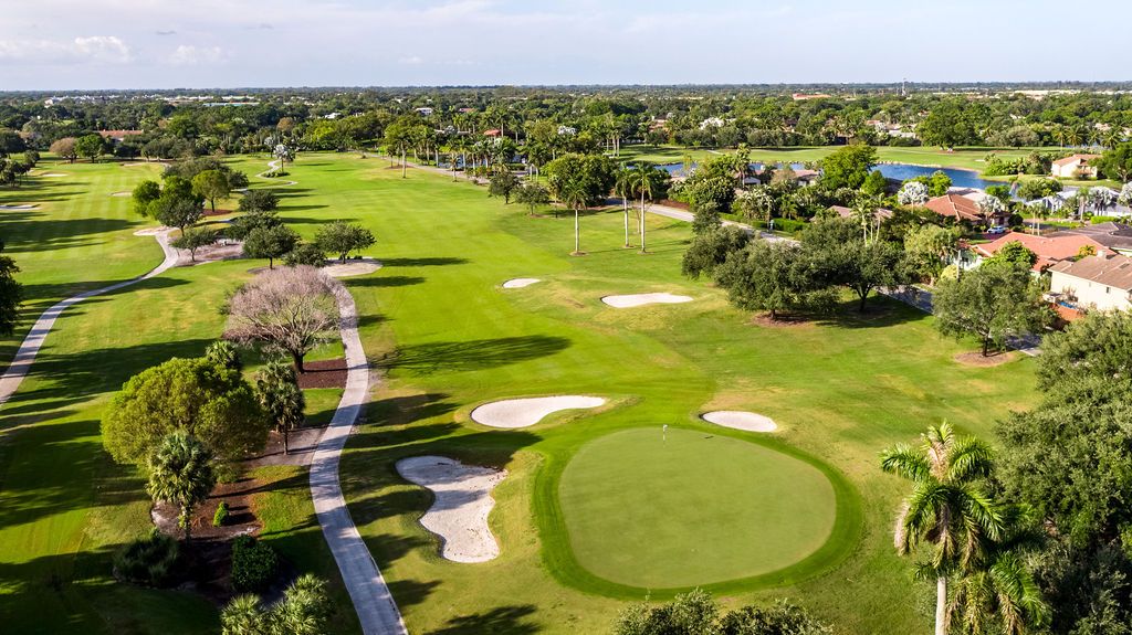 Aerial panoramic view of a lush golf course with palm trees, sand traps and manicured fairways stretching into the distance.