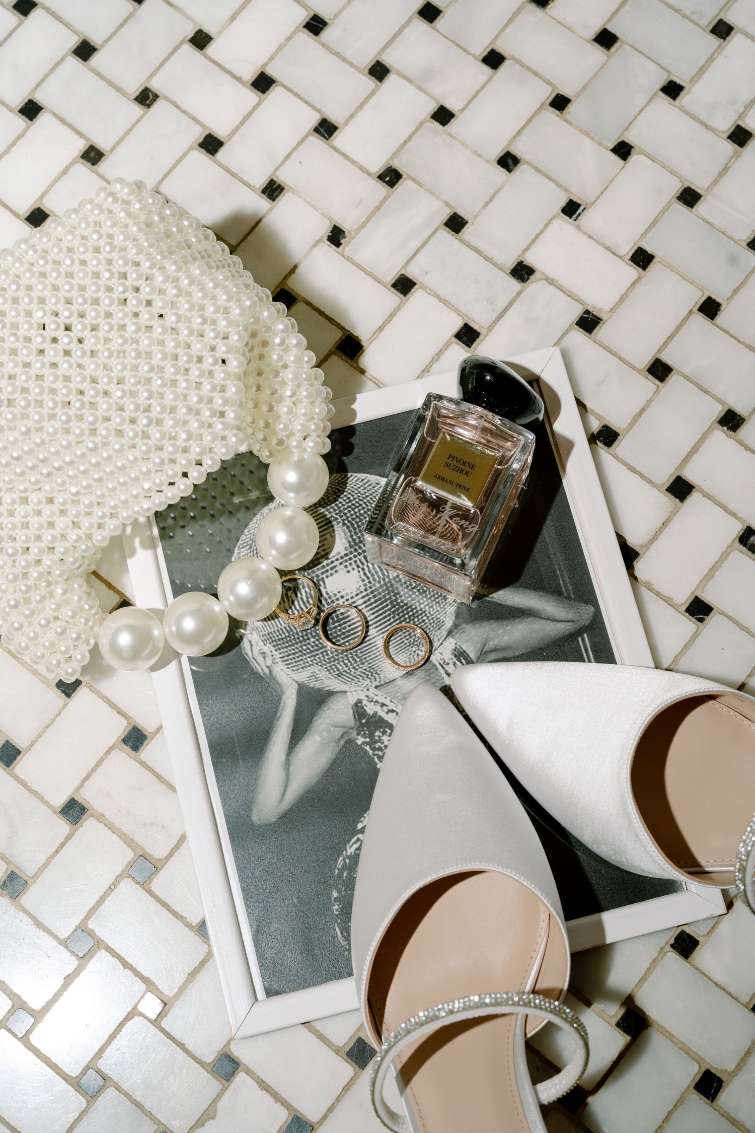 Wedding accessories including pearls, perfume bottles, and shoes arranged on a white lattice surface.