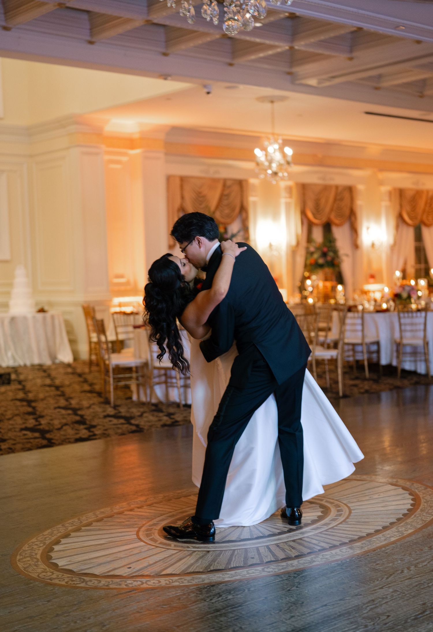 A romantic first dance between newlyweds in an elegant ballroom with chandeliers and soft lighting.