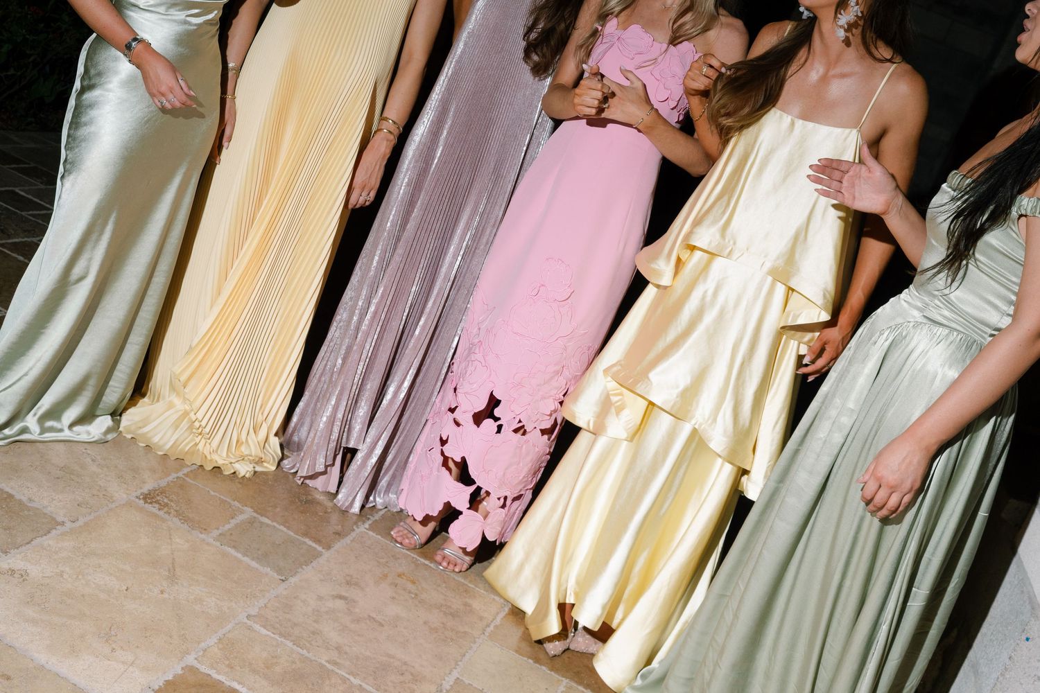 Five bridesmaids in mismatched pastel gowns in sage, lavender, pink, yellow, and gold standing together.