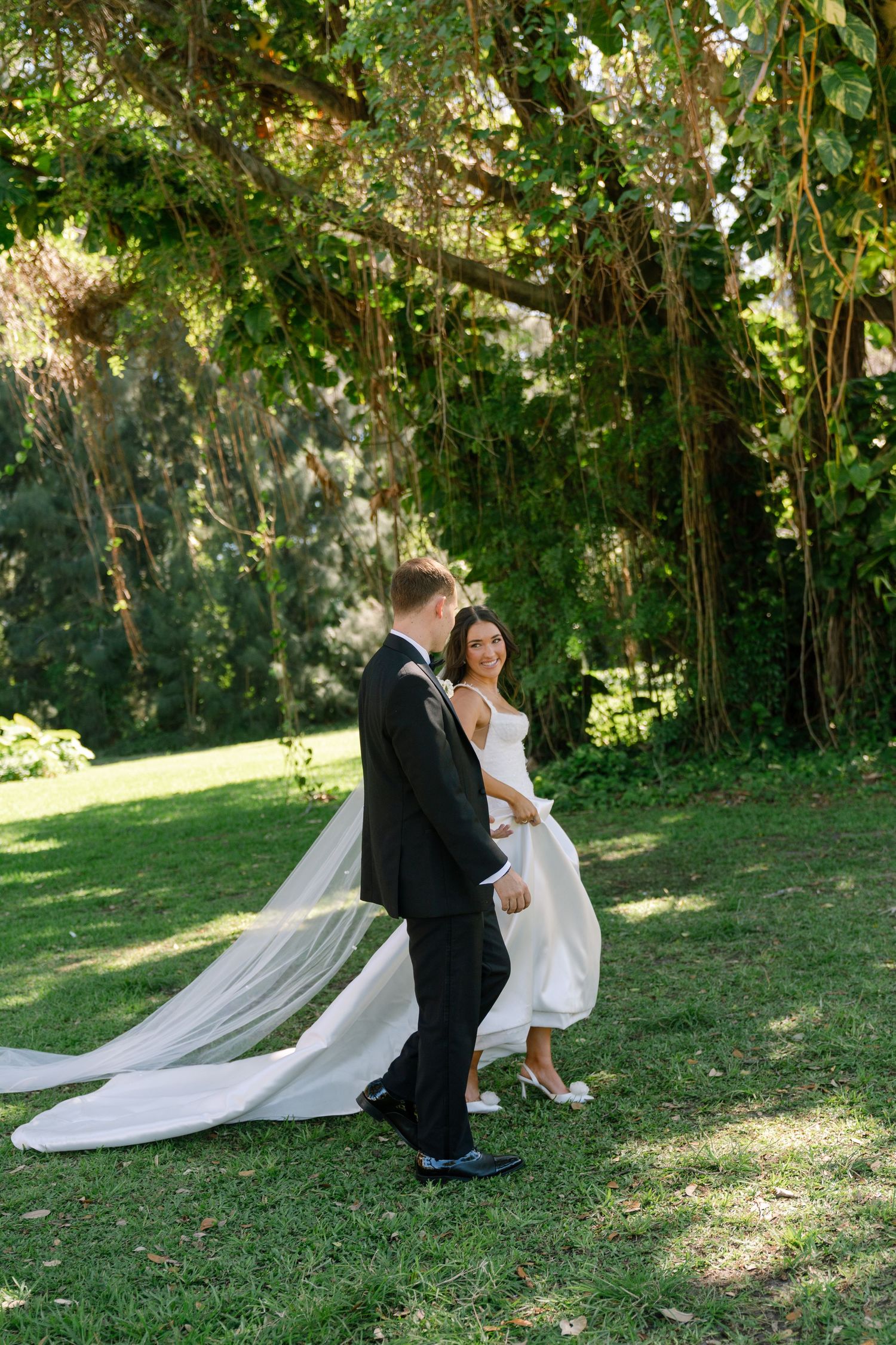 Bride and groom walking hand in hand through lush green garden on their wedding day.